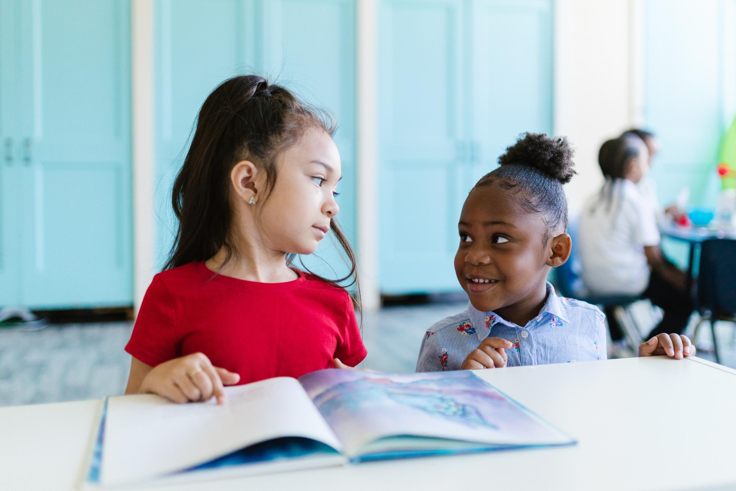 two girls sitting side by side and reading
