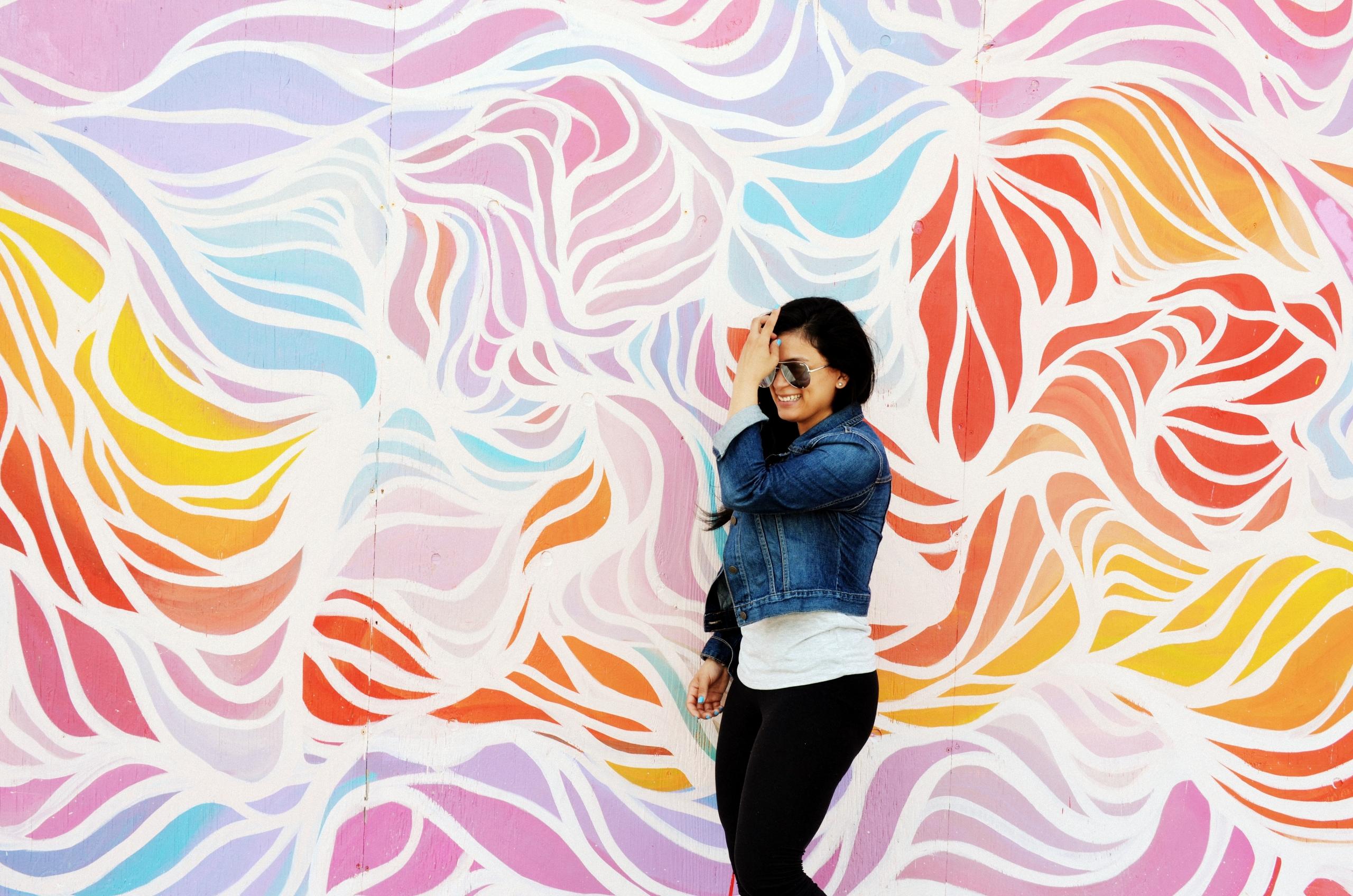 woman walking in front of wall with brightly coloured mural painted on it