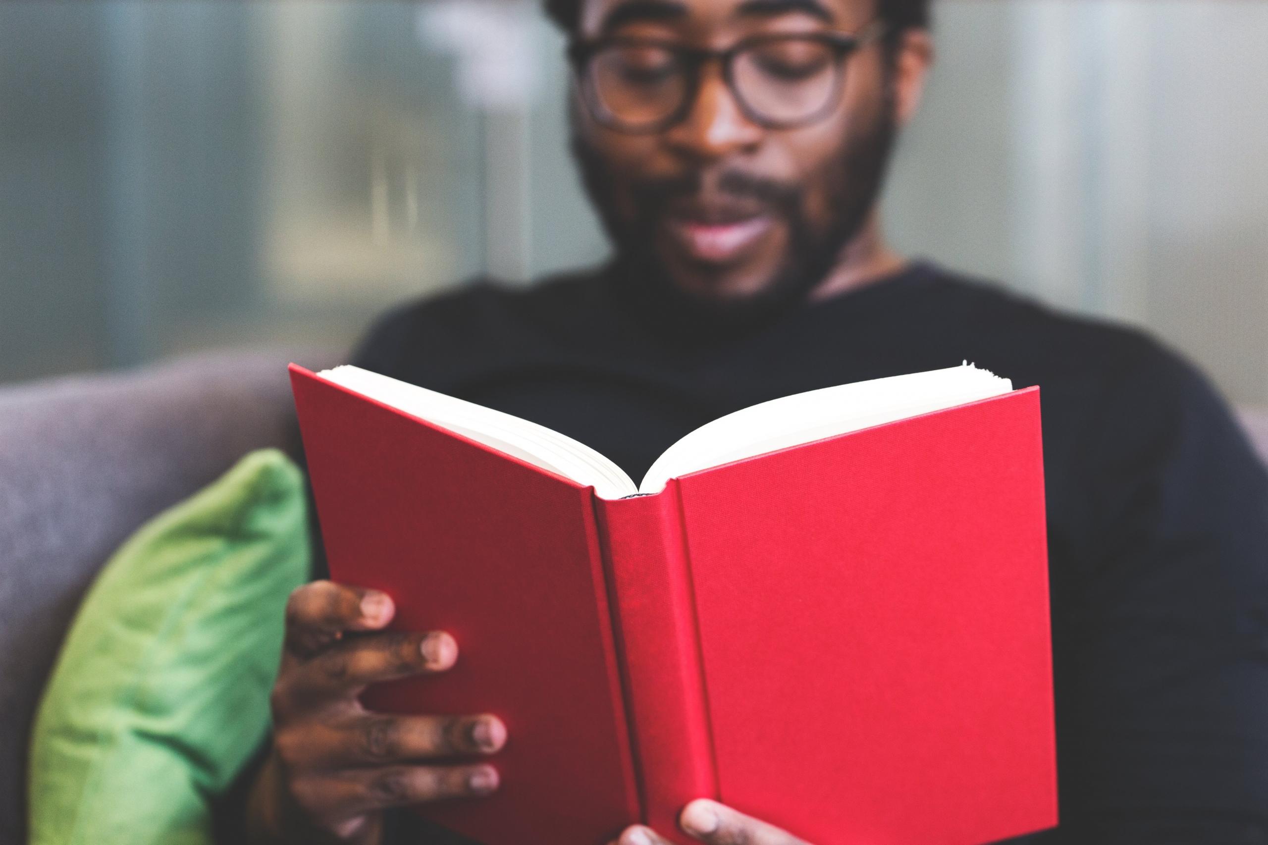 person sitting on chair reading a red hardcover book
