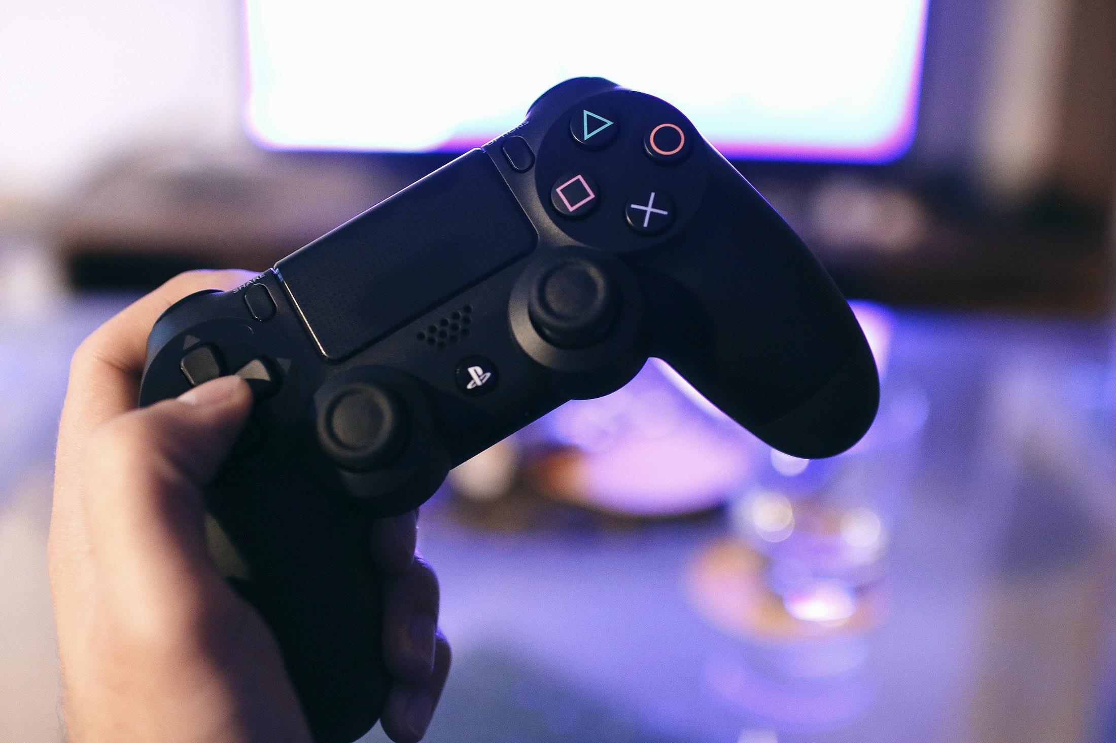 person holding black game controller in front of tv screen