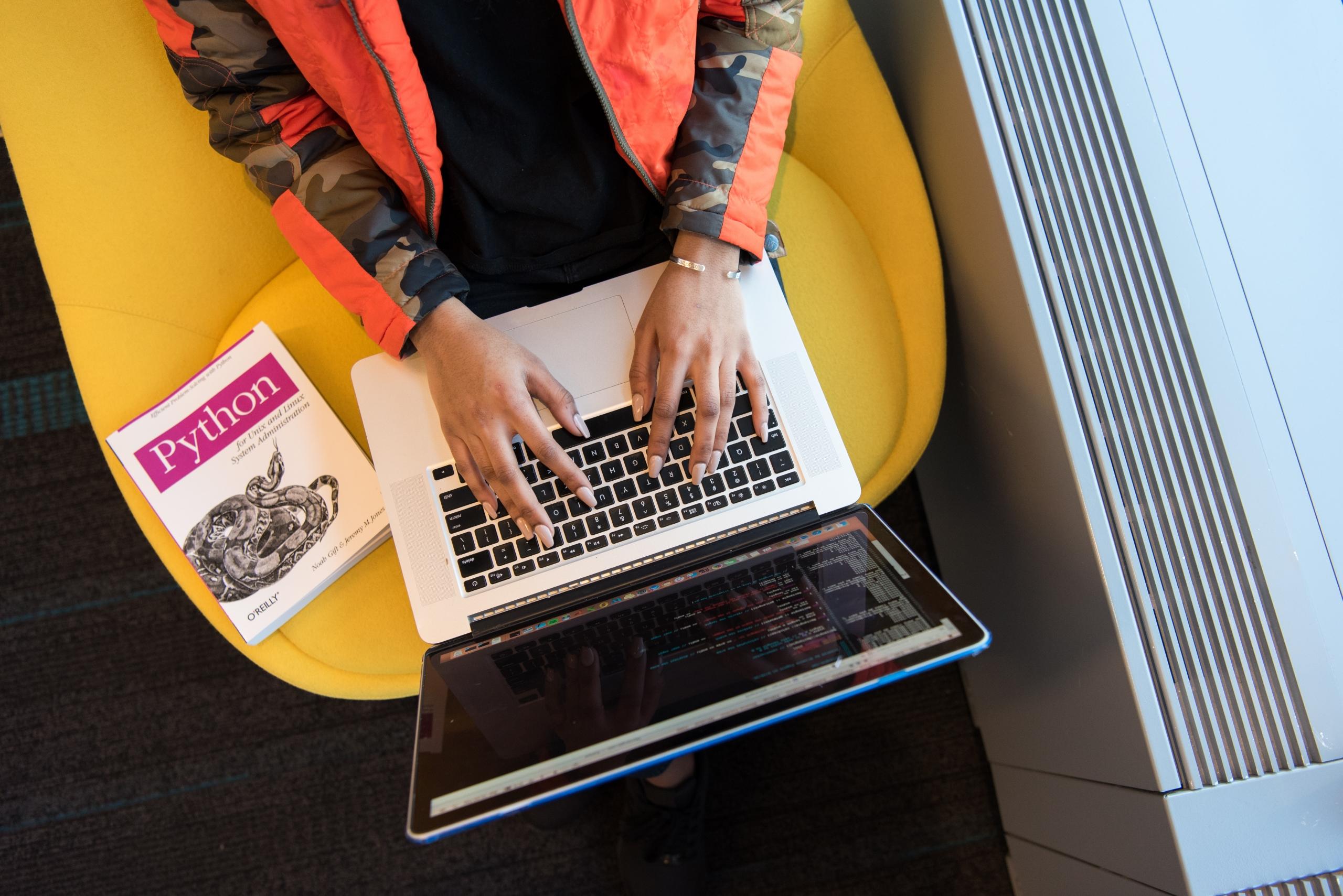 person coding Python with guidebook placed on chair