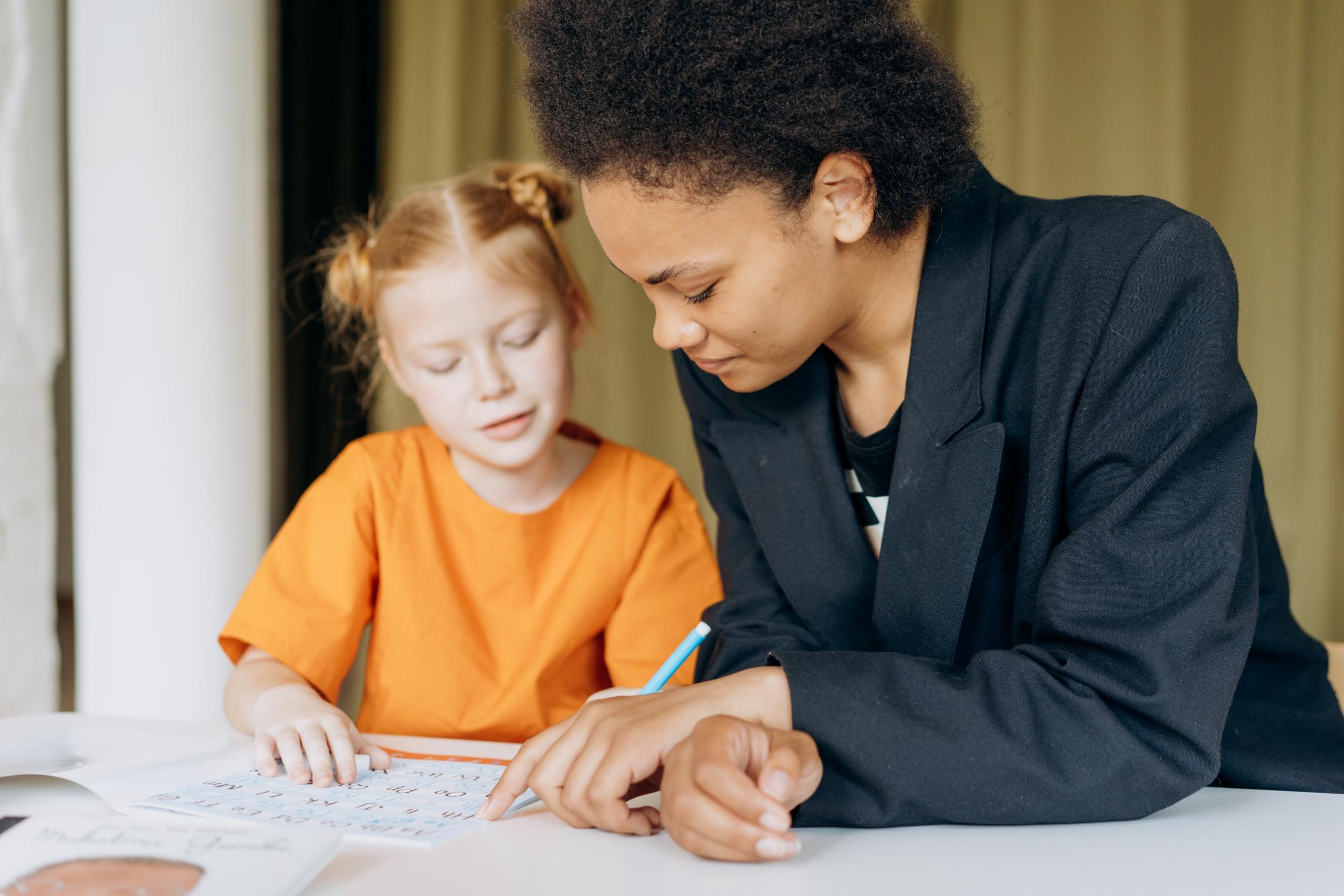 school girl and teacher sitting at same table completing a classwork exercise
