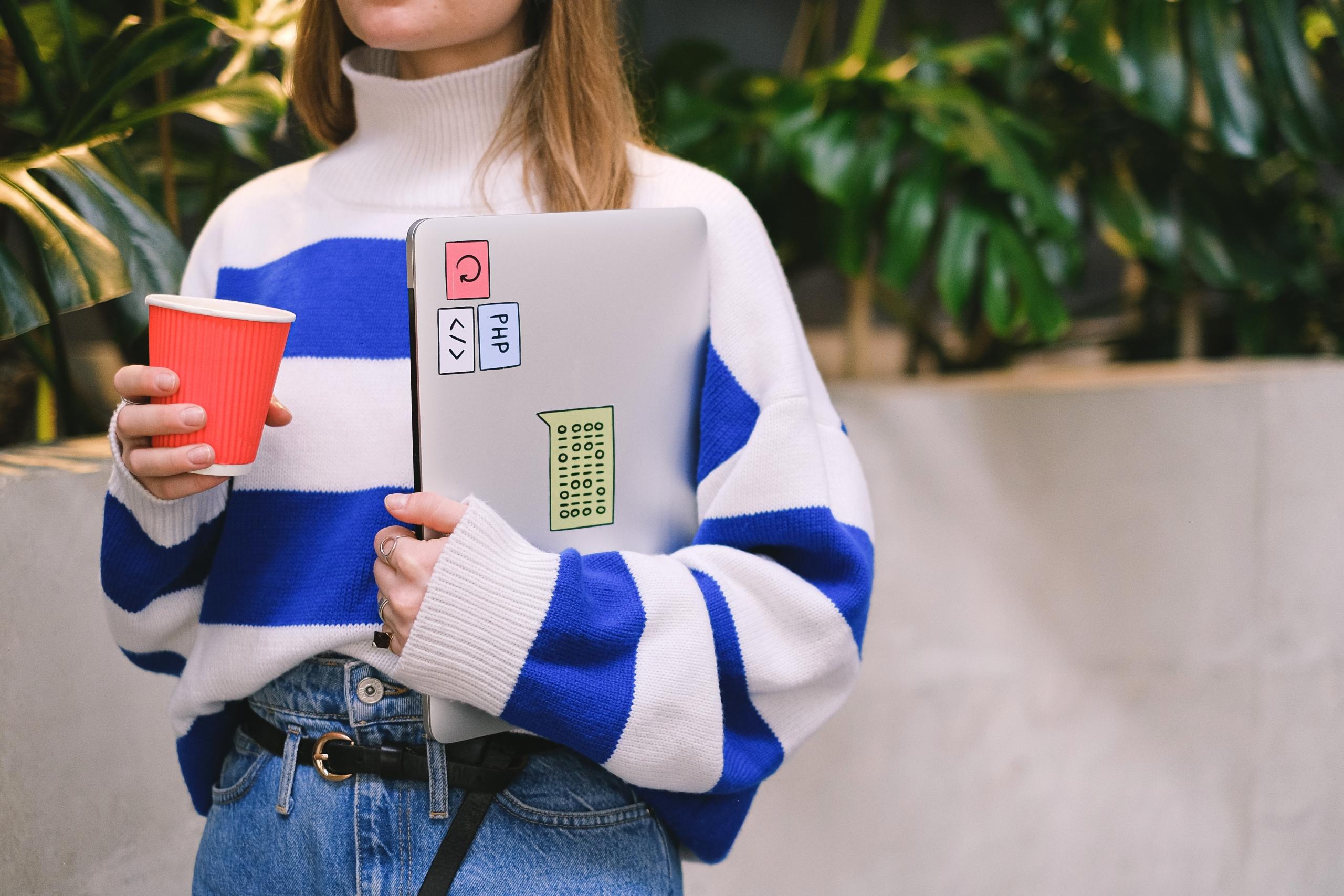 person holding coffee cup and laptop decorated with PHP stickers