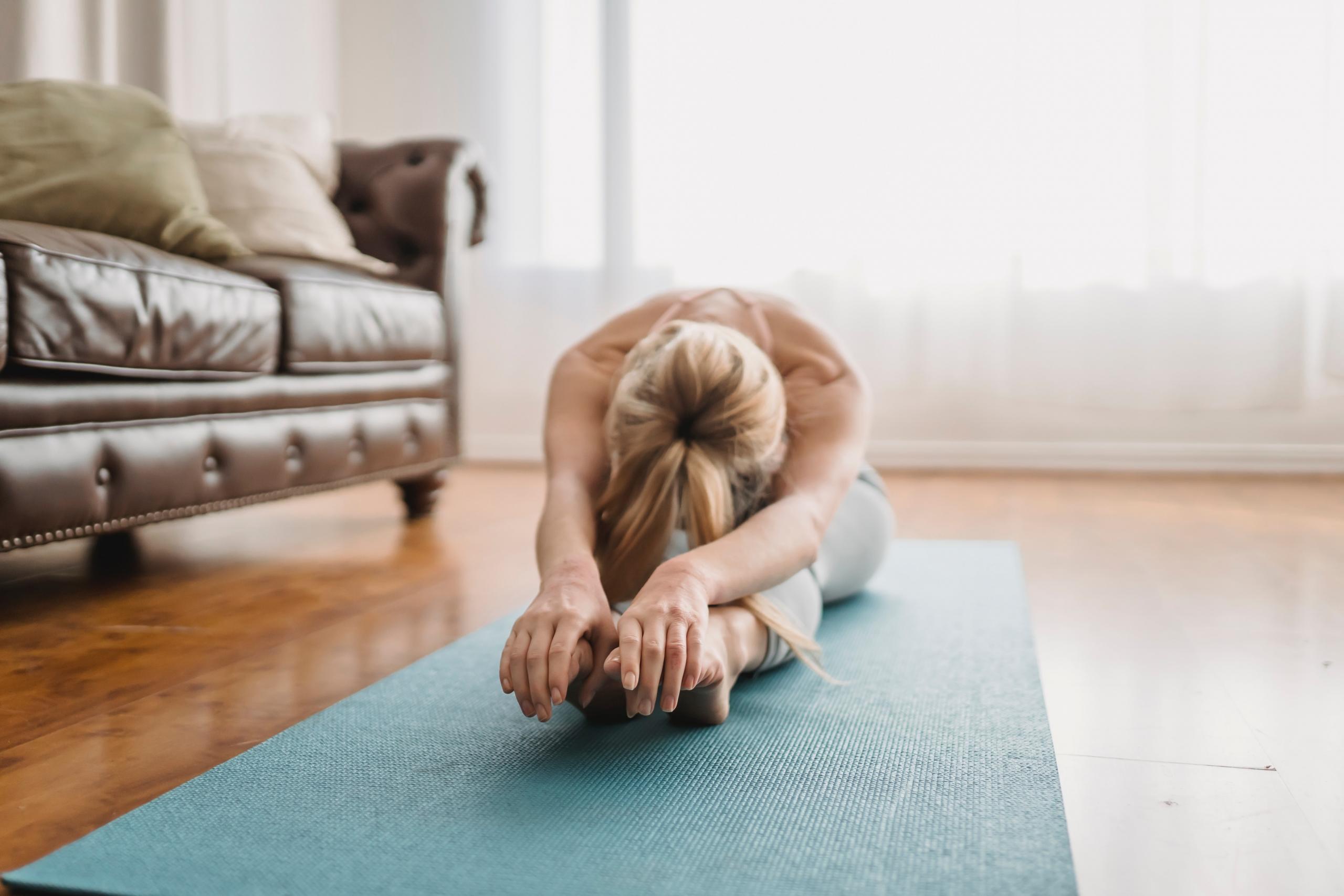 person doing forward bend on yoga mat in living room