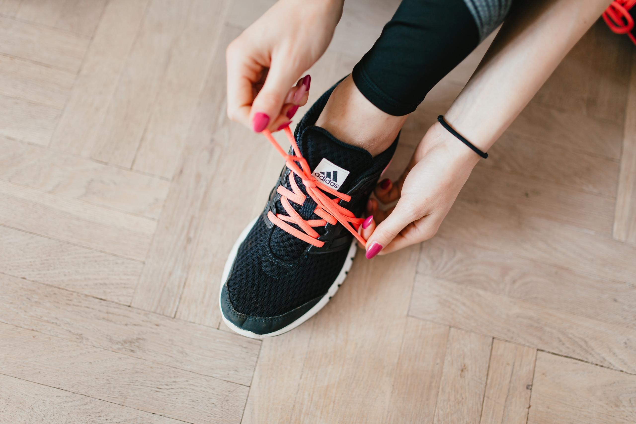 person with pink nail polish tying the laces of sports trainers