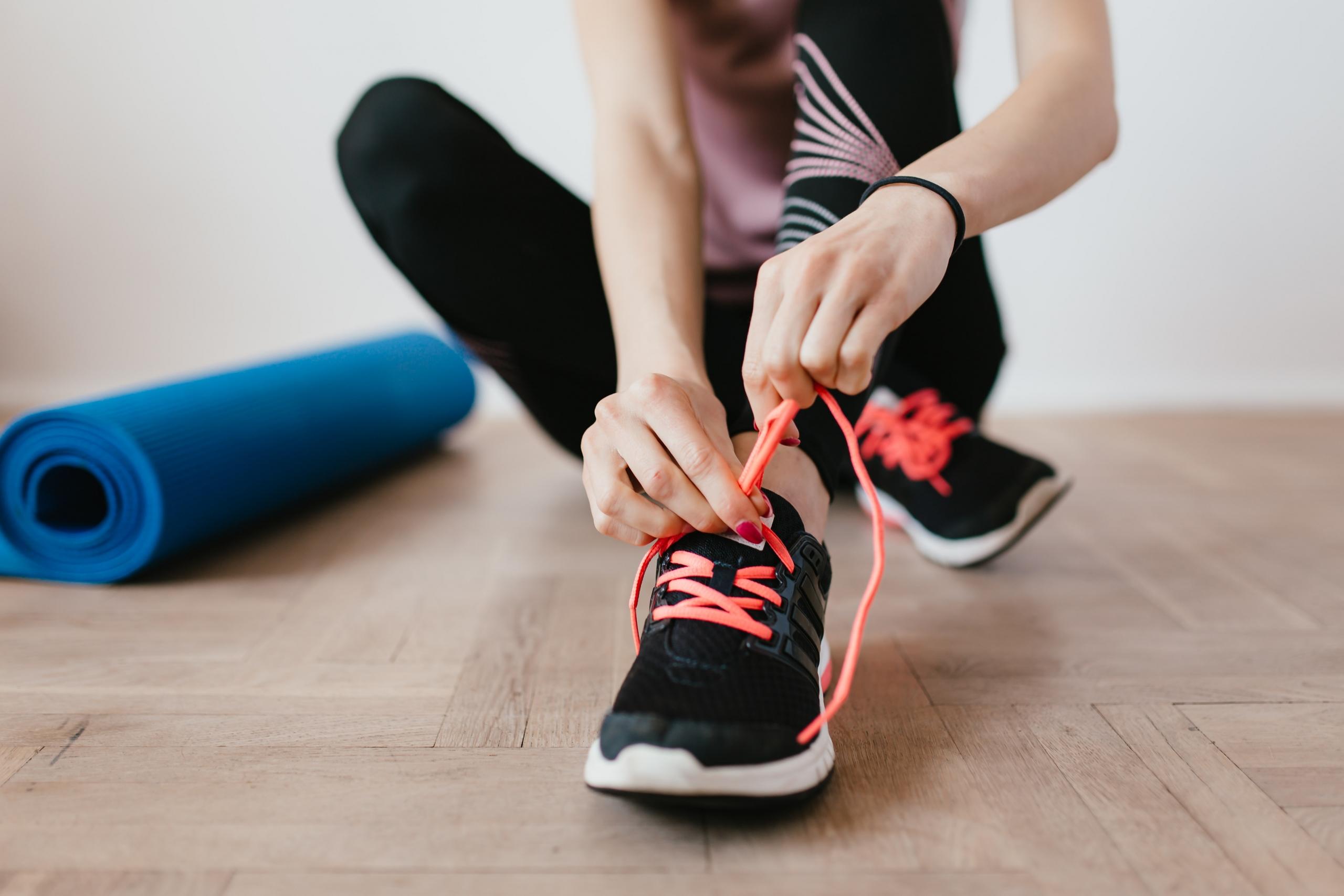 person tying sports shoe laces sitting next to yoga mat