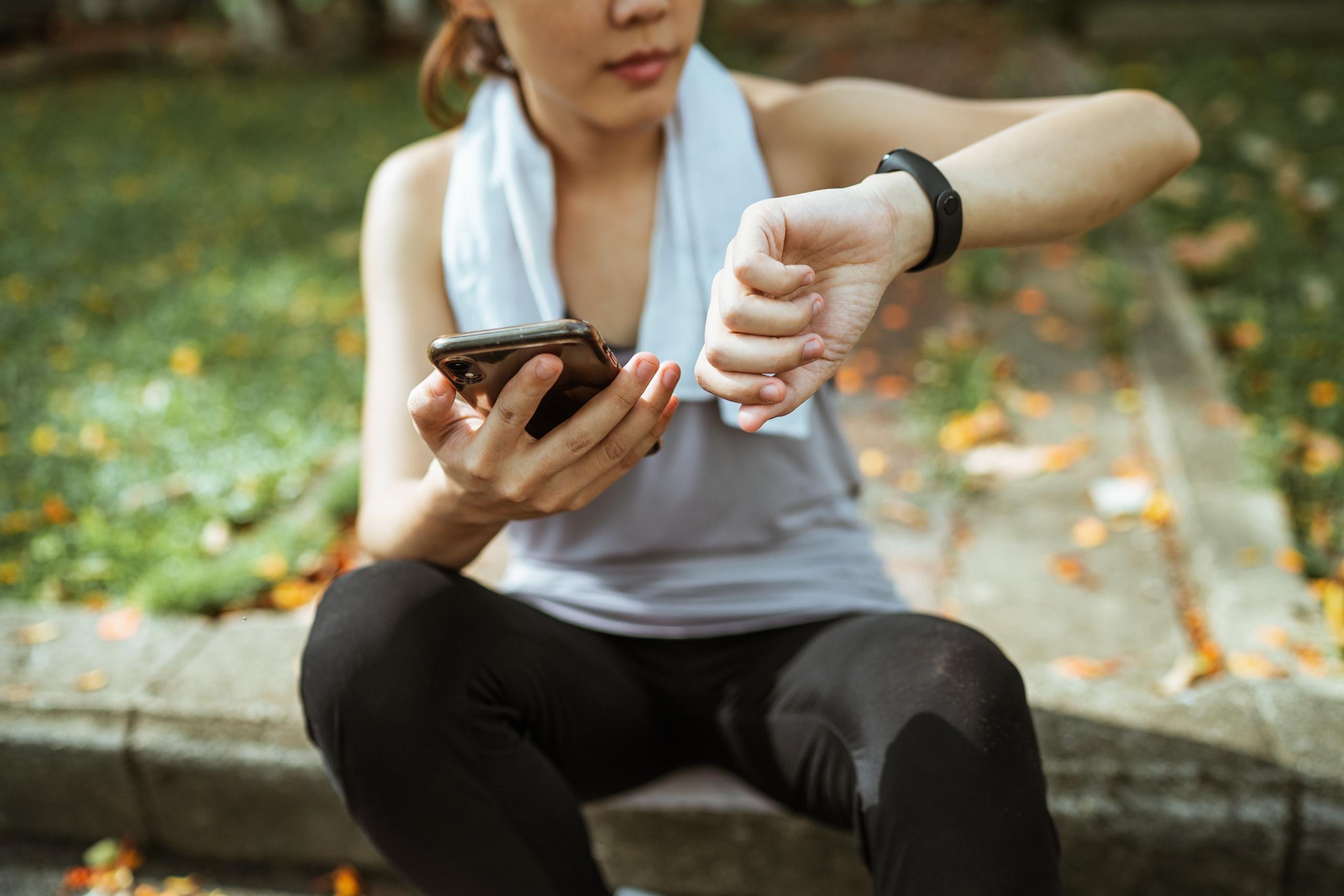 runner sitting on kerb looking at sports watch and phone