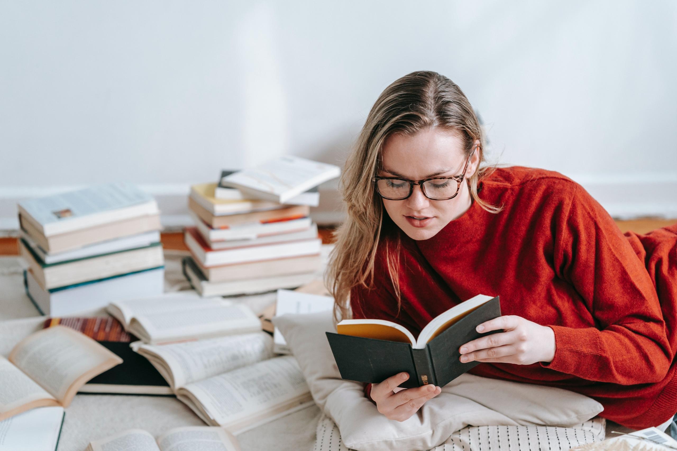 person wearing red pullover lying amongst a pile of books