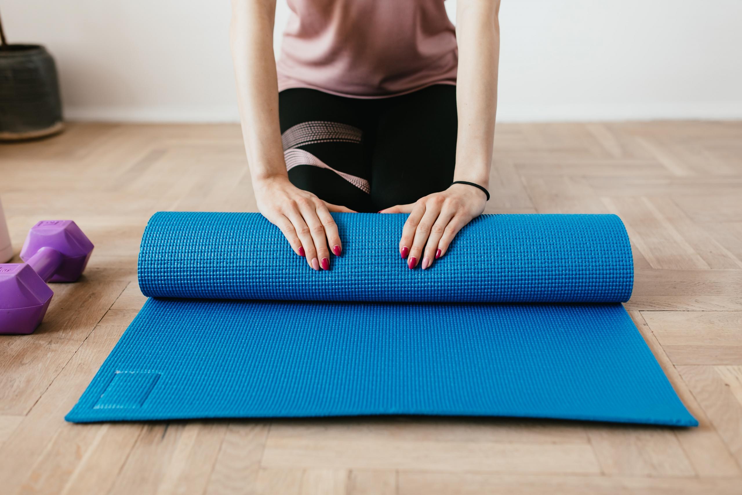 person unrolling blue yoga mat next to purple dumb bells