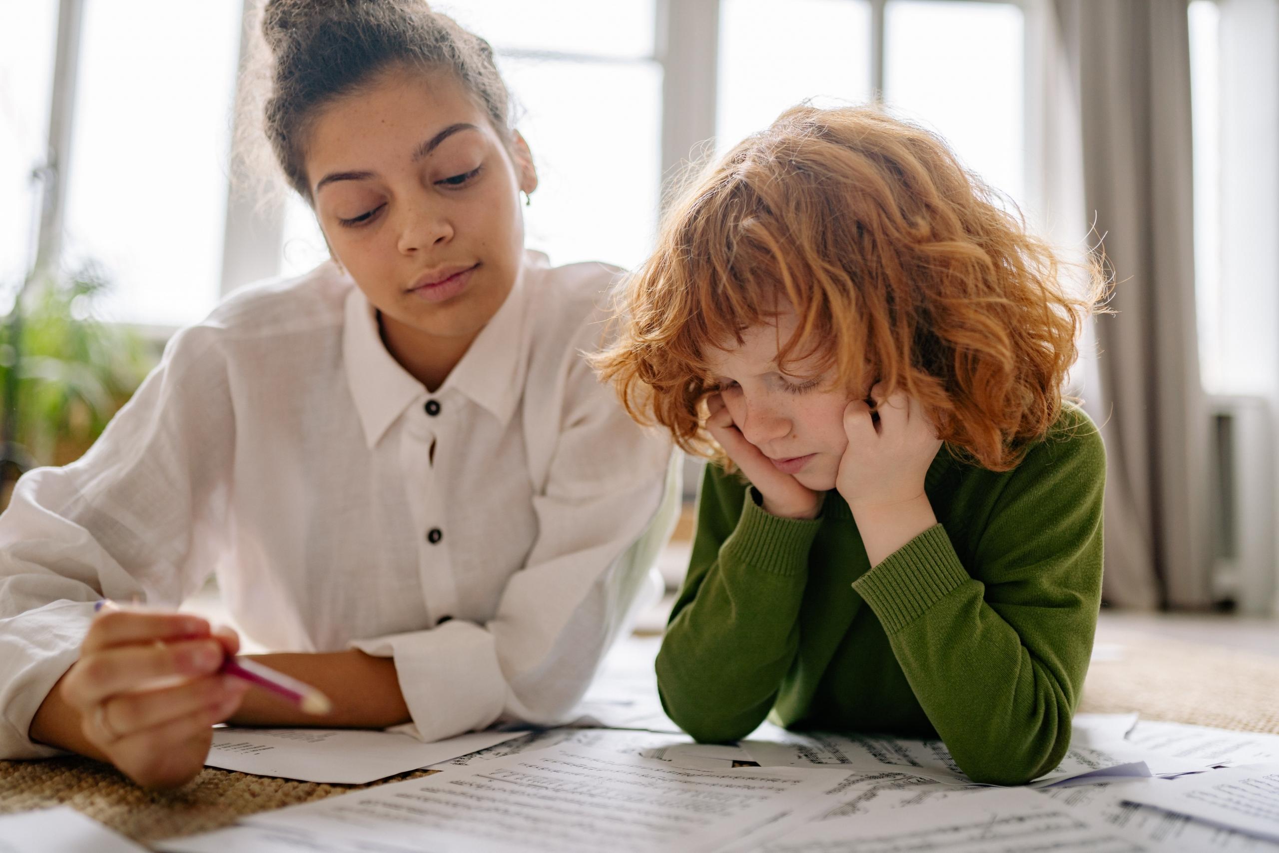 child and teacher lying on the living room floor working through worksheets together
