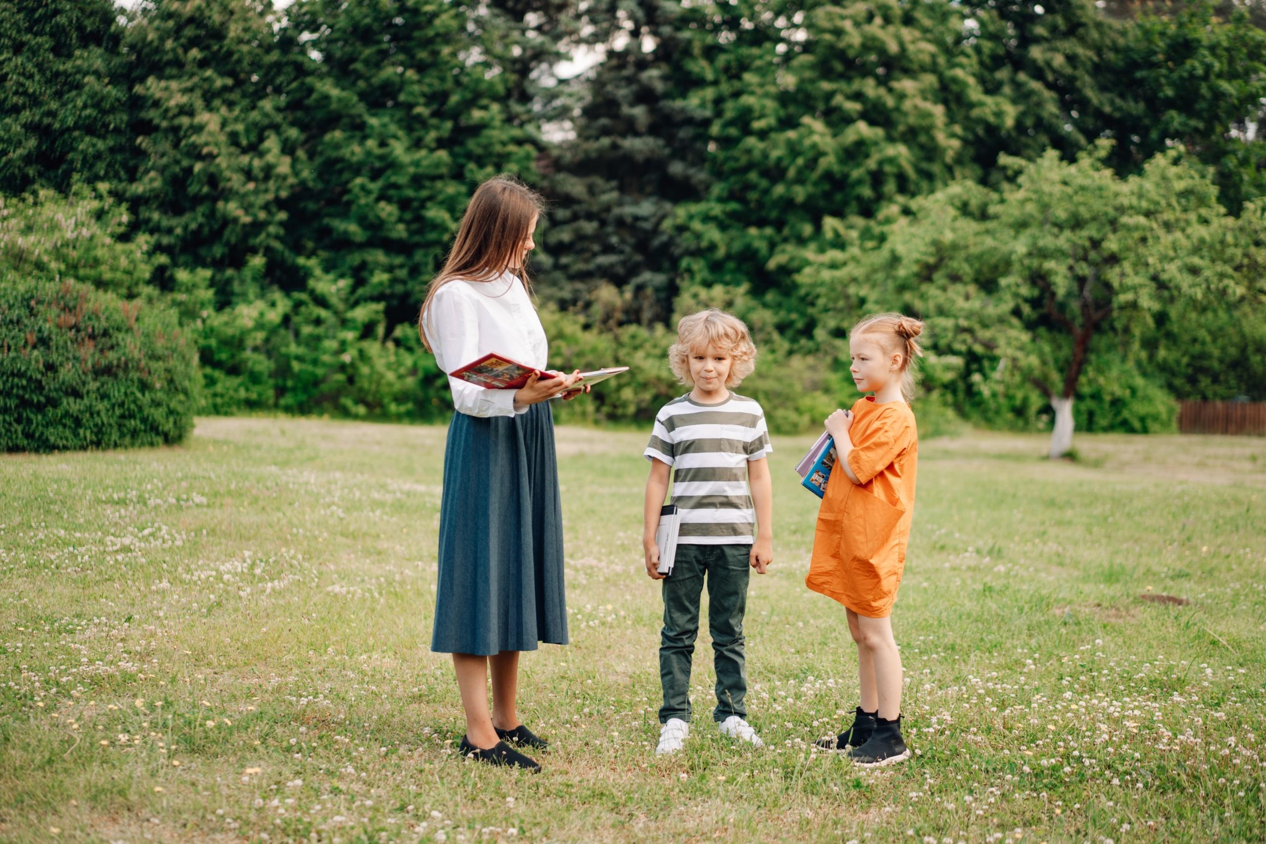 woman standing in a garden reading a book to two children