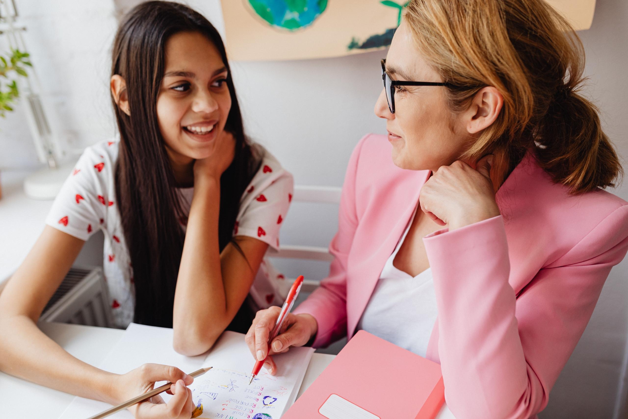 girl doing homework with tutor at white desk