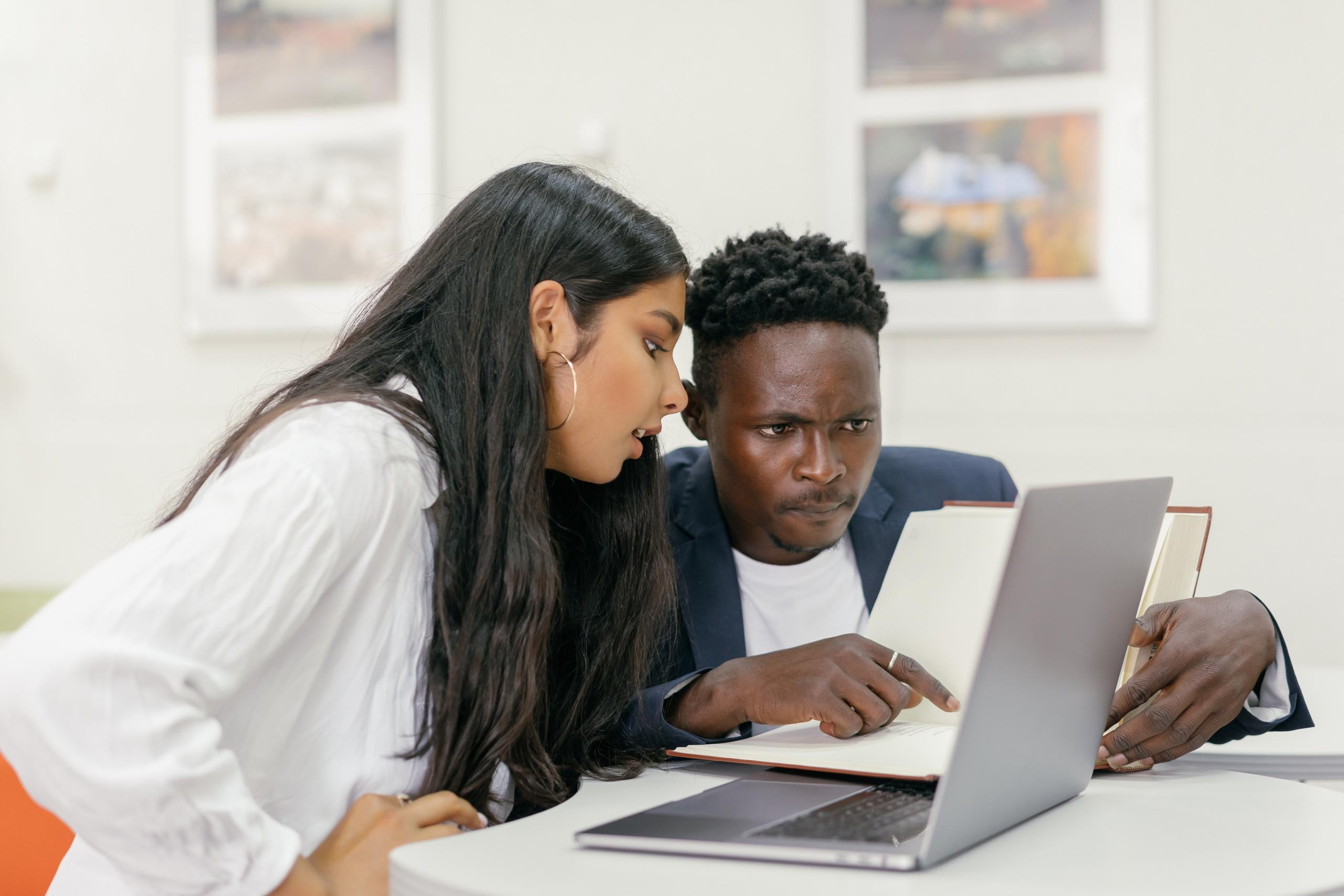 teacher checking student's work in notebook and on laptop