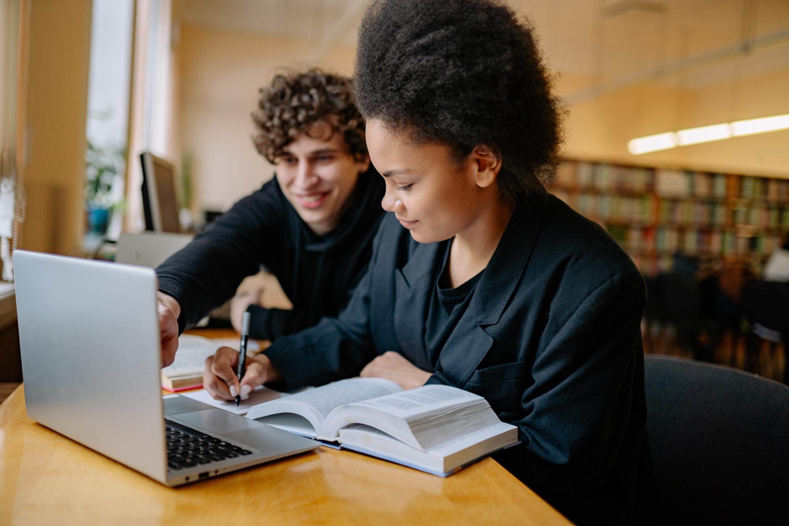 tutor and student smiling sitting side by side at desk in library