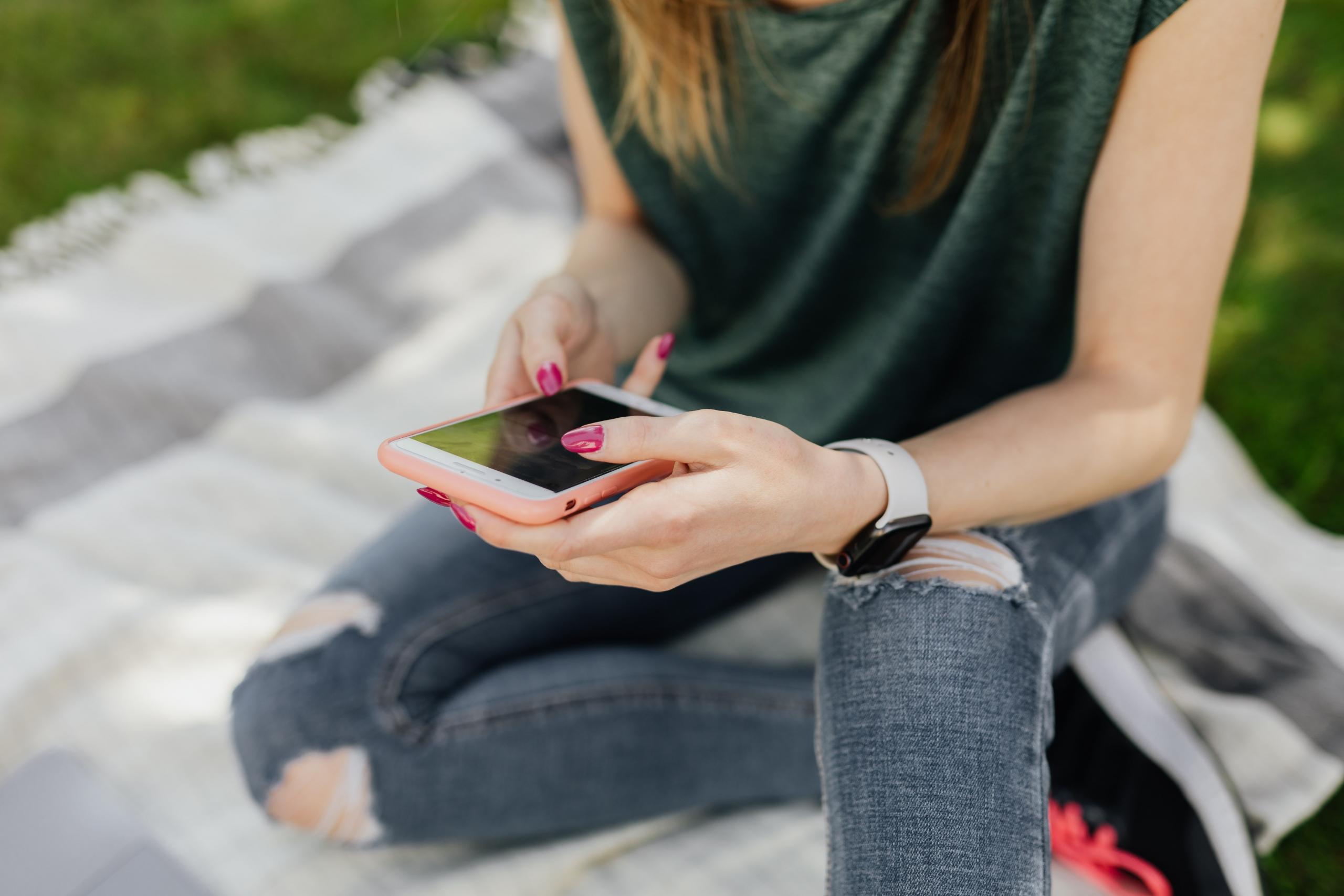 person sitting on picnic blanket scrolling through smartphone