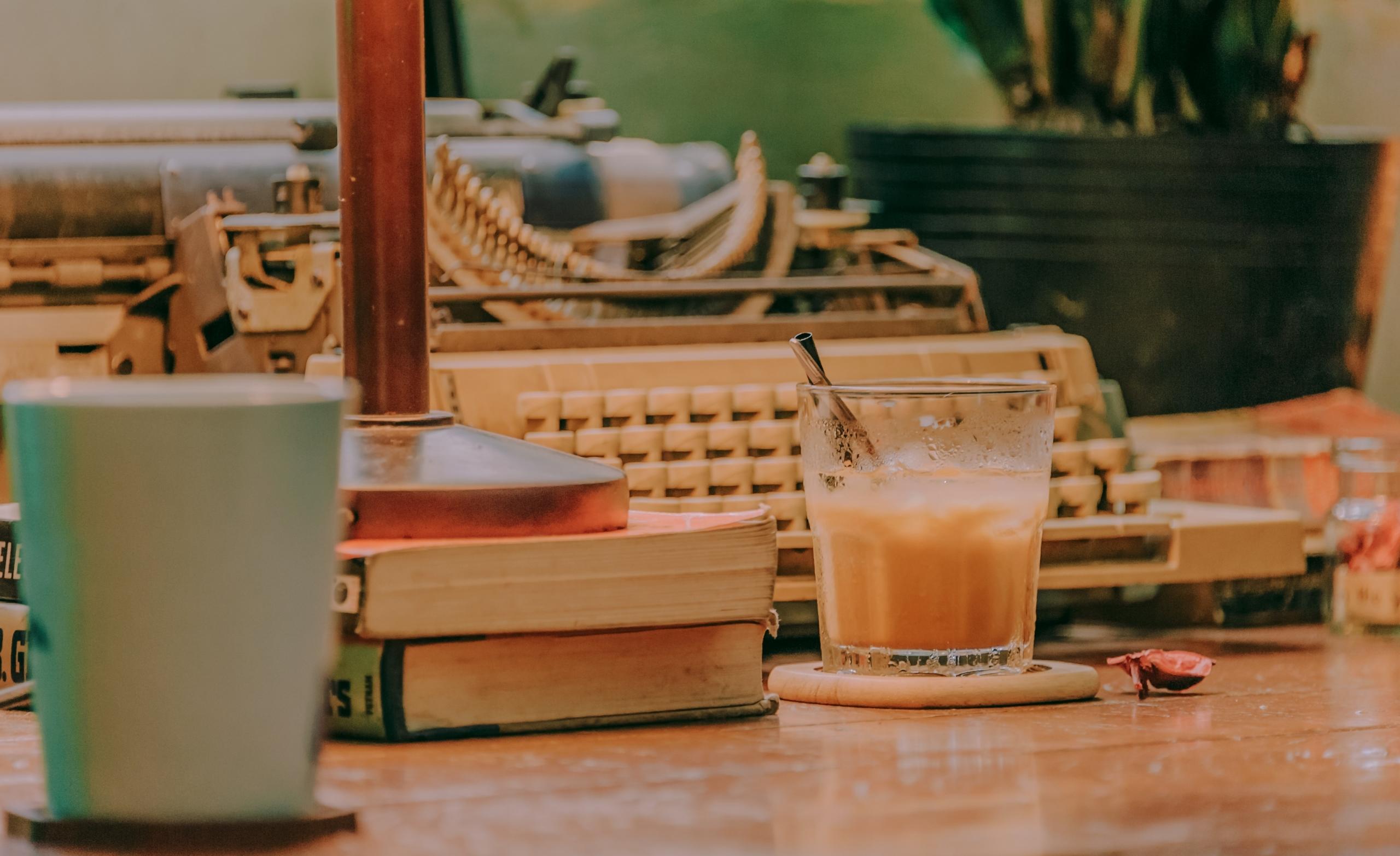 glass of iced coffee on desk in front of old typewriter
