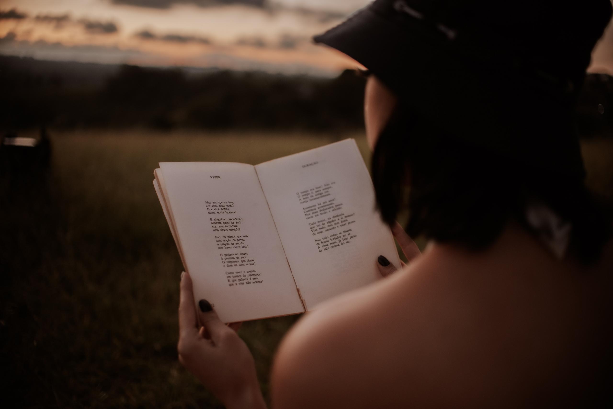 woman sitting outside at dusk reading a book of poems