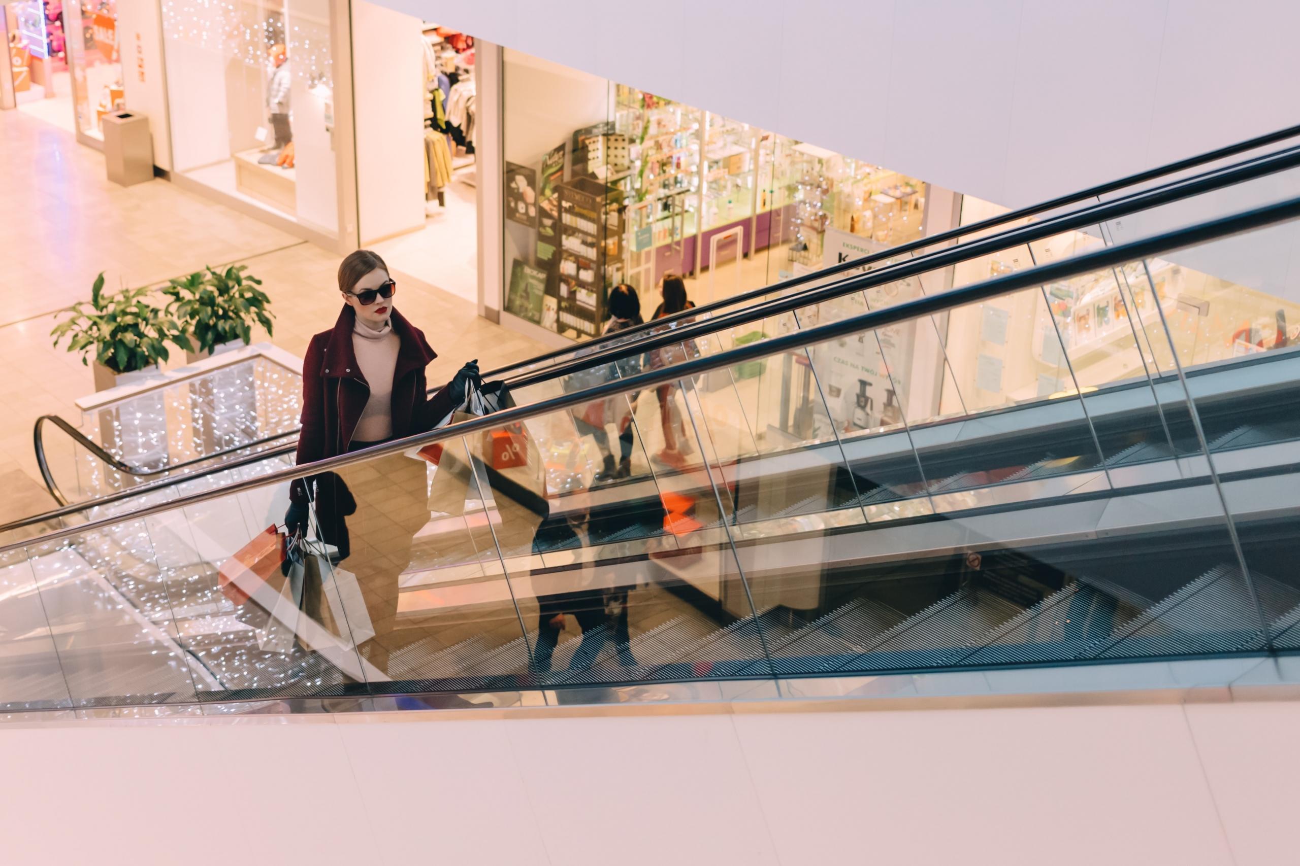 woman carrying shopping bags riding escalator in shopping mall