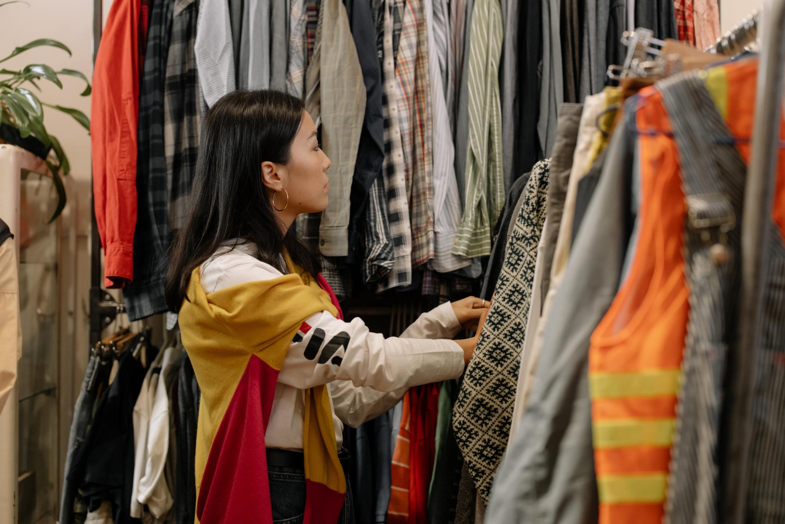 woman browsing through clothes on rails in second-hand shop