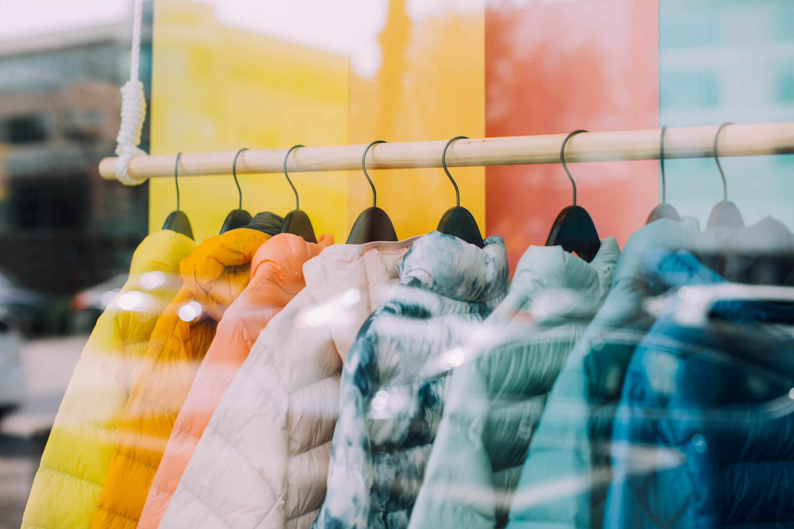 multicoloured puffy coats on hangers in shop display window