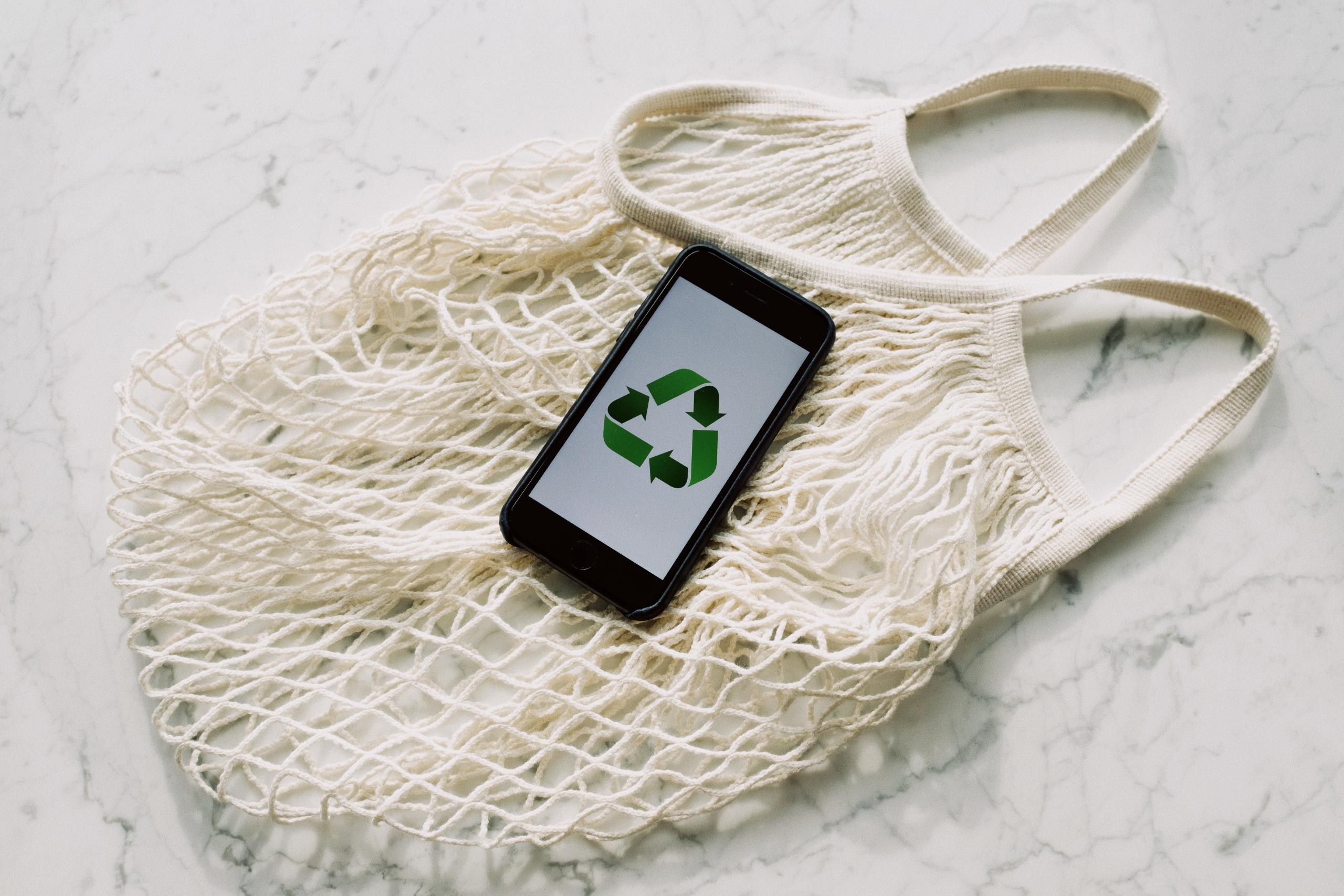 woven cotton market bag under cellphone displaying image of recycling symbol