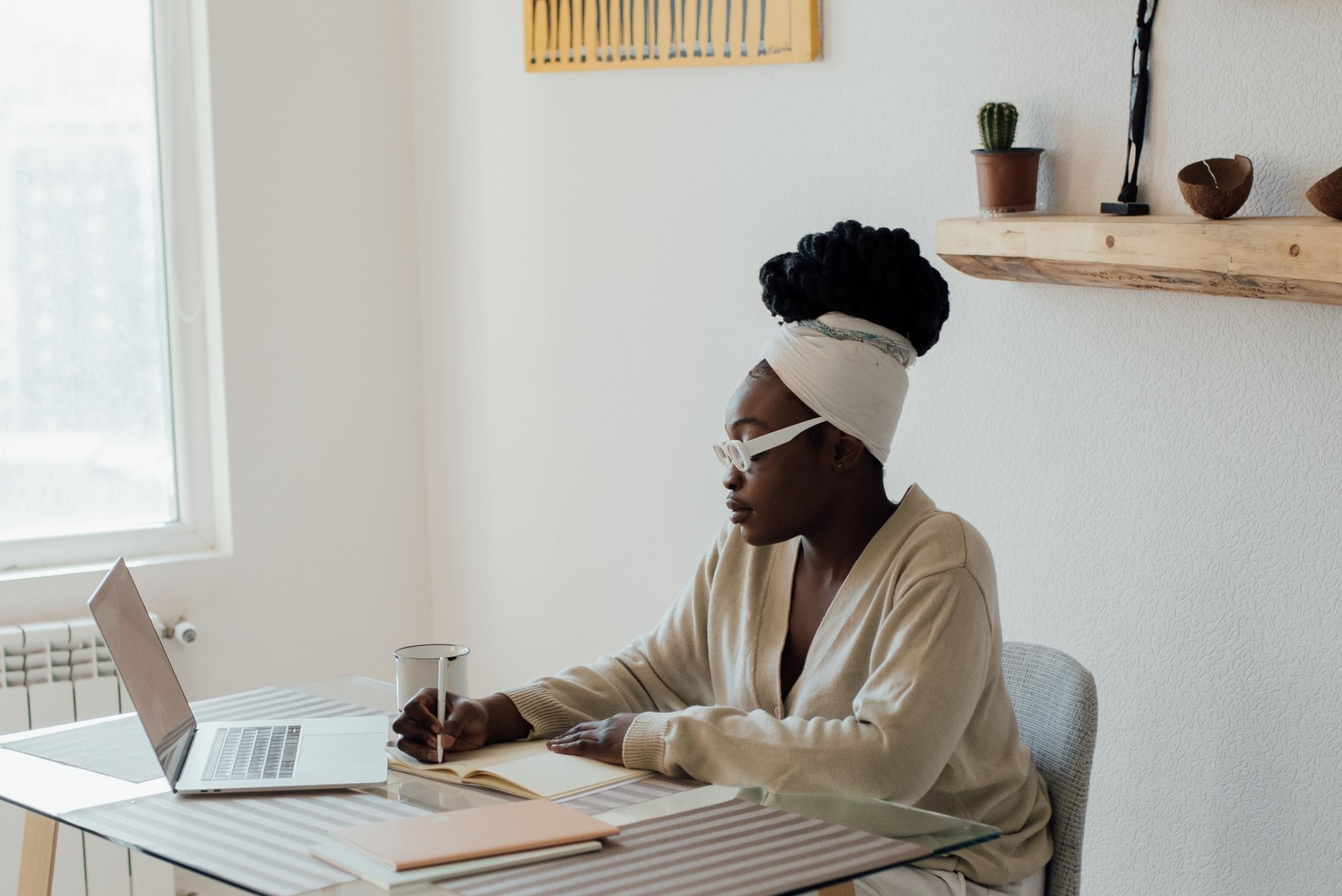 woman seated at table making notes and using laptop