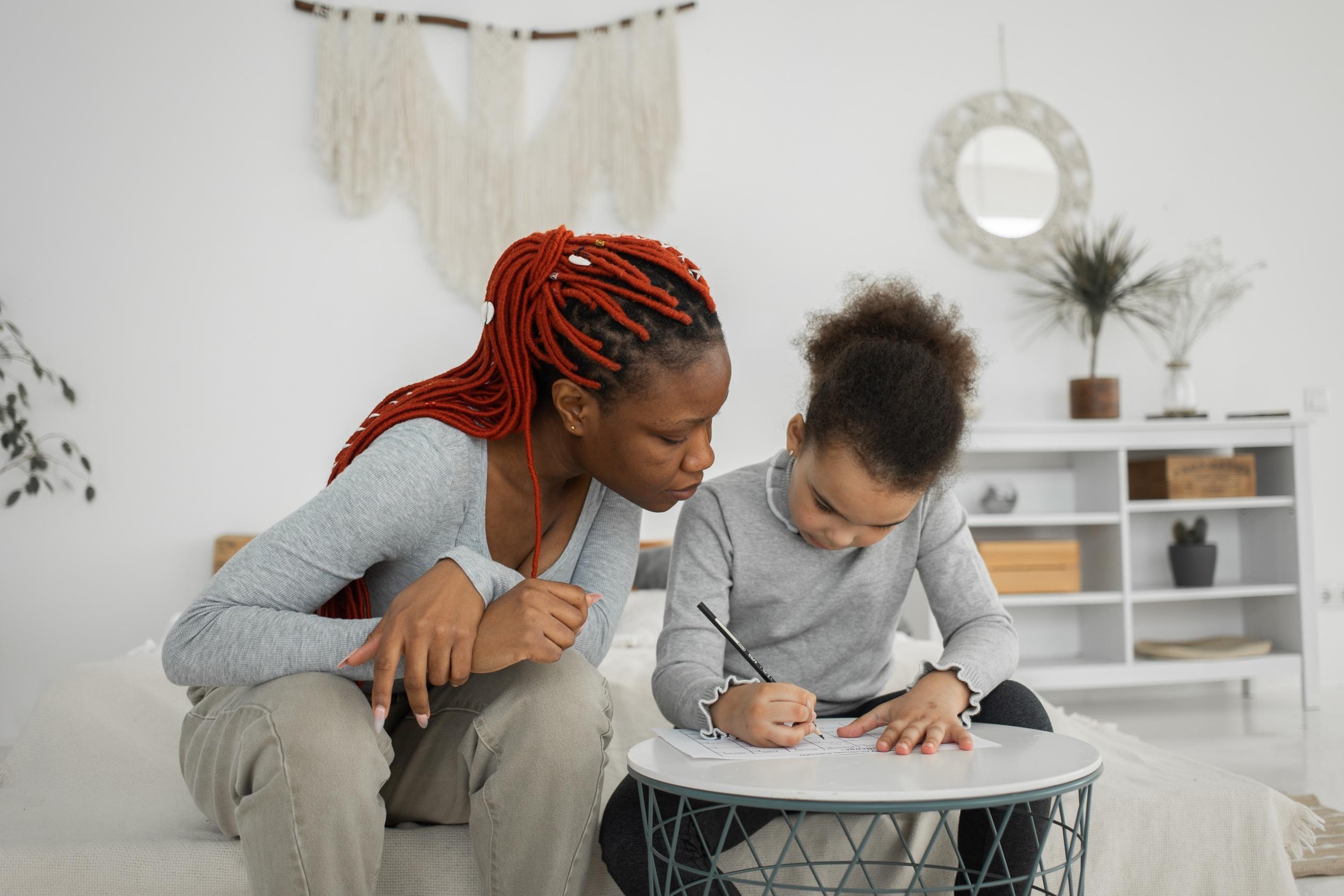girl doing homework on sofa while private teacher looks on