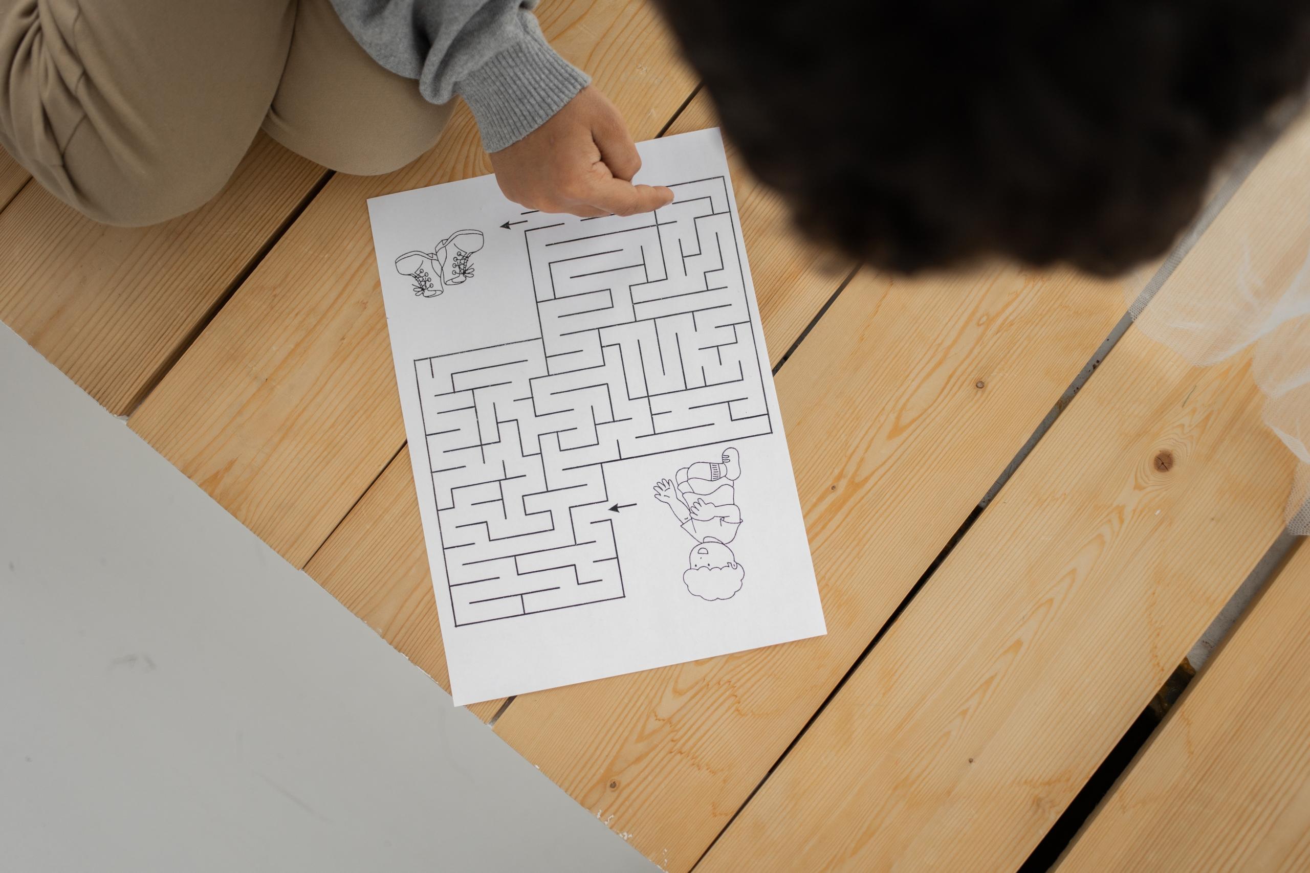 child using finger to trace solution to puzzle on sheet of paper