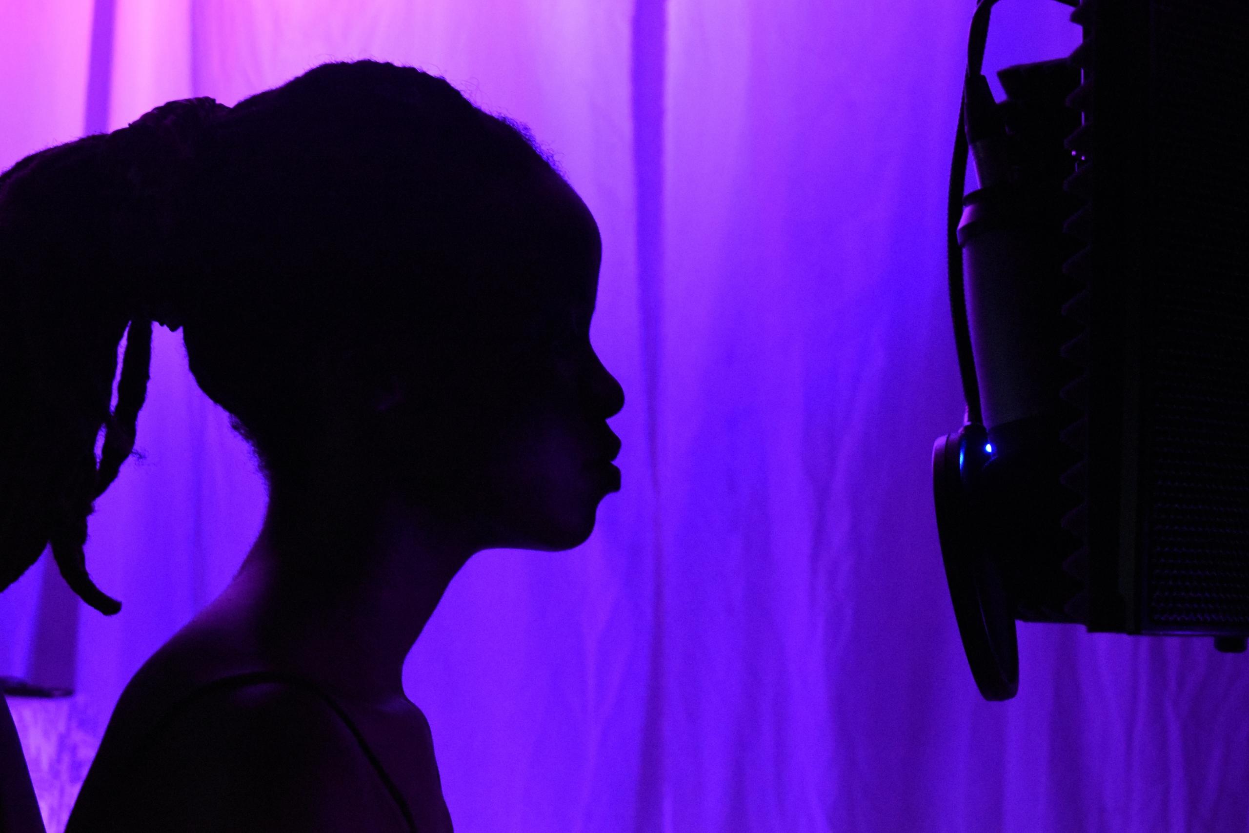 silhouette of person in front of mic, with purple background
