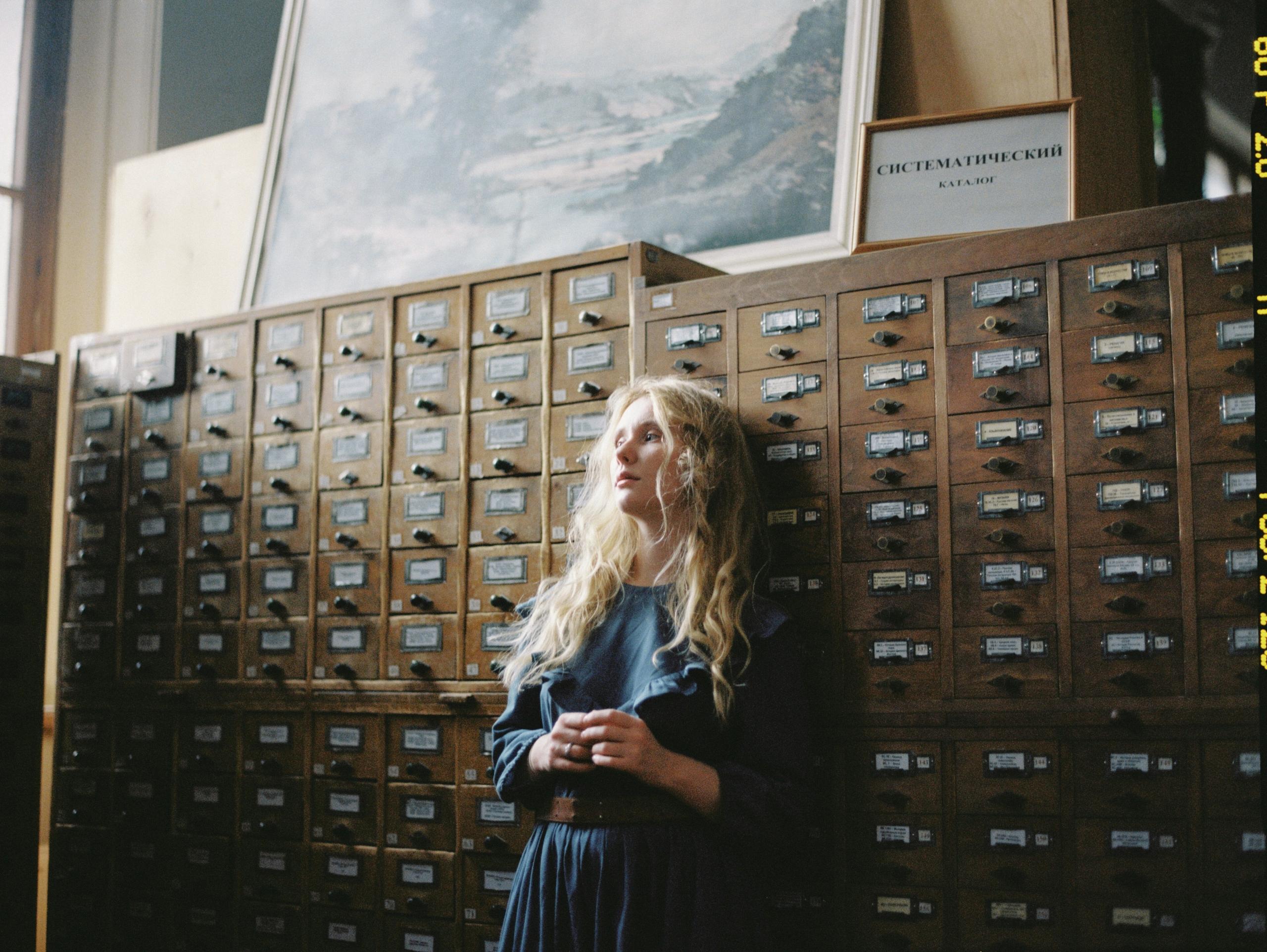 woman deep in thought leaning against apothecary cabinet with labelled drawers