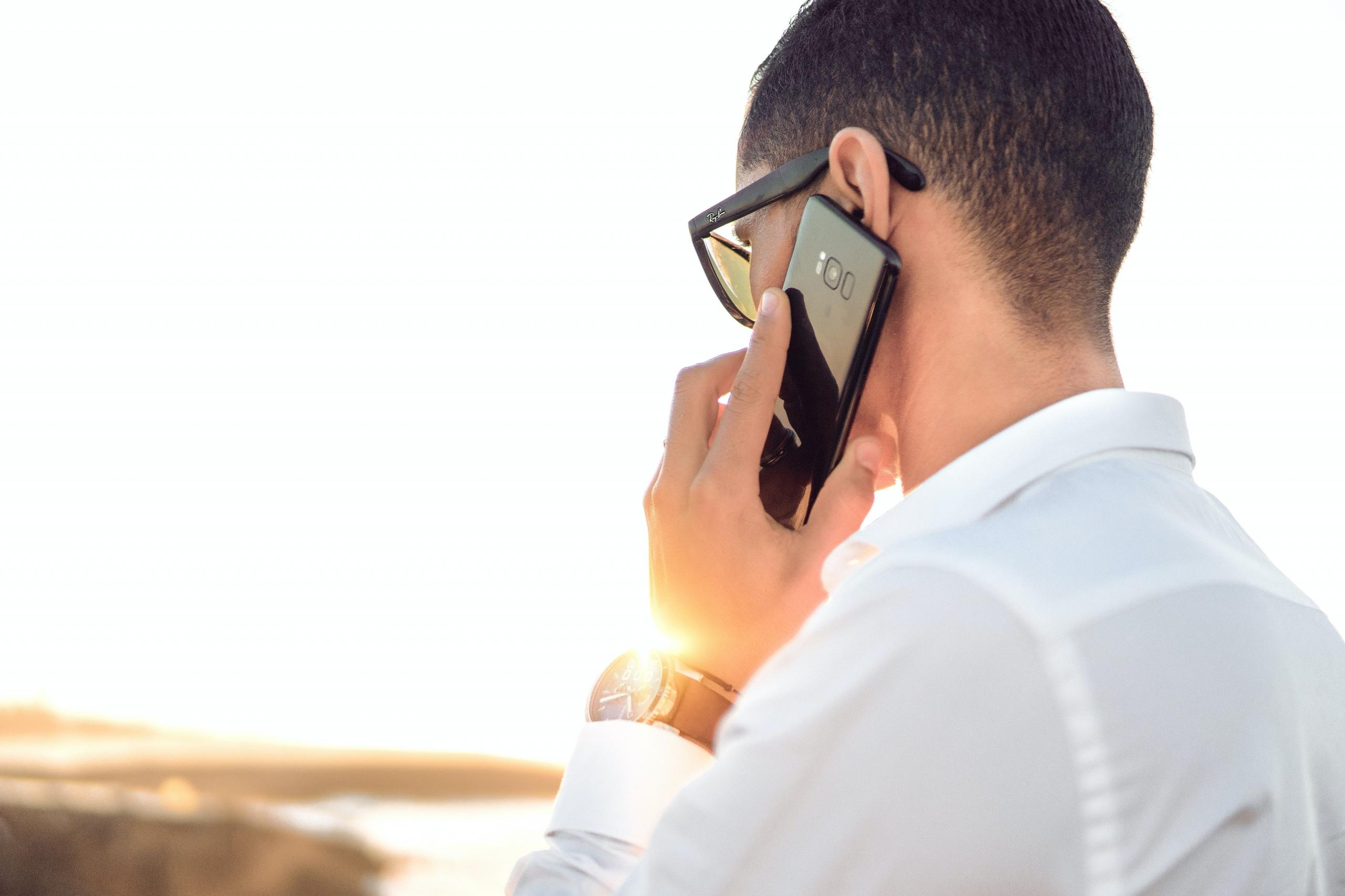 man talking on smartphone outdoors at sunset