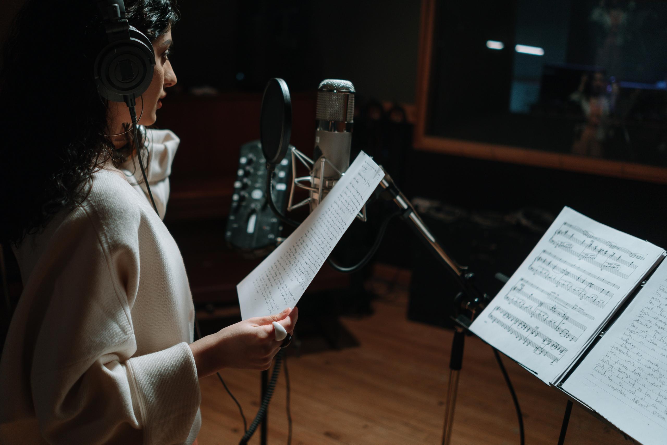 woman singing into microphone in recording studio, holding lyric sheet