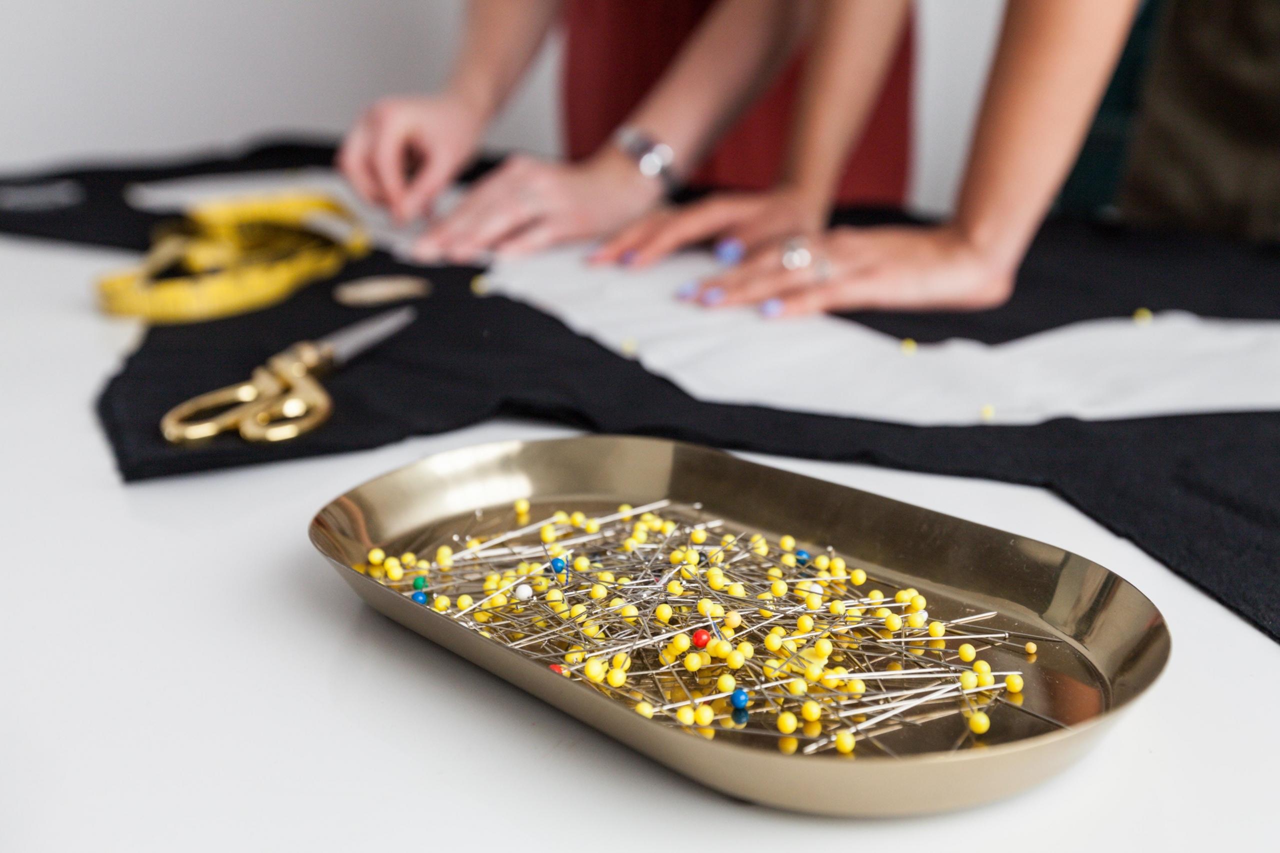 seamstresses cutting and pinning garment using sewing template and straight pins