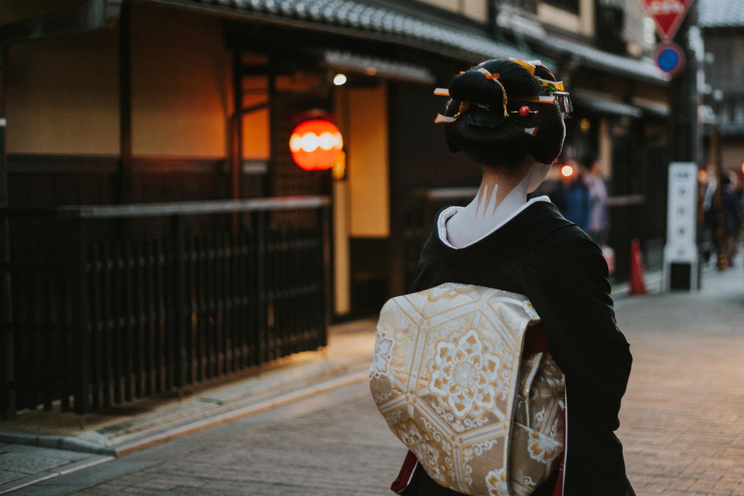 geisha in traditional dress seen from behind in a street at dusk