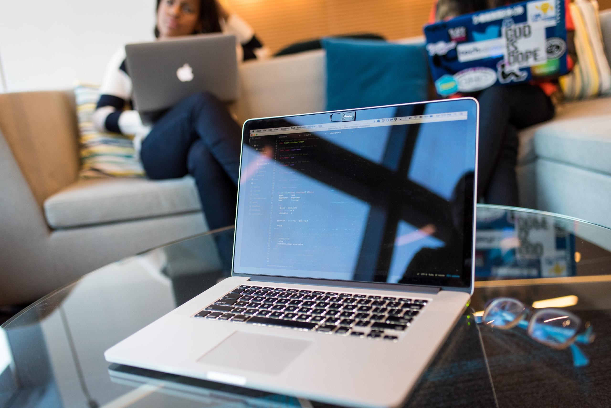 colleagues seated around coffee table coding using laptops