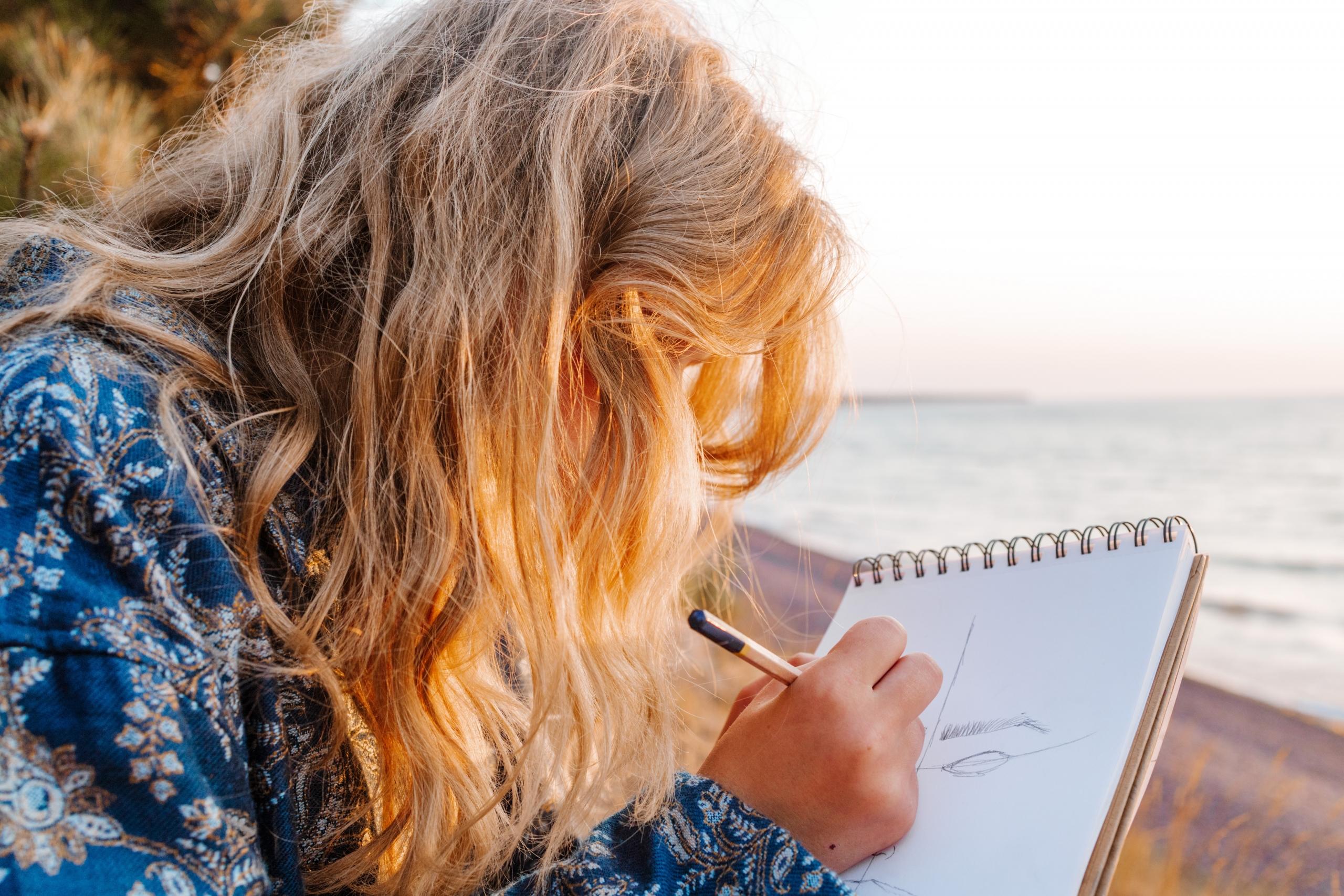 person sitting on the beach at dusk sketching on sketch pad