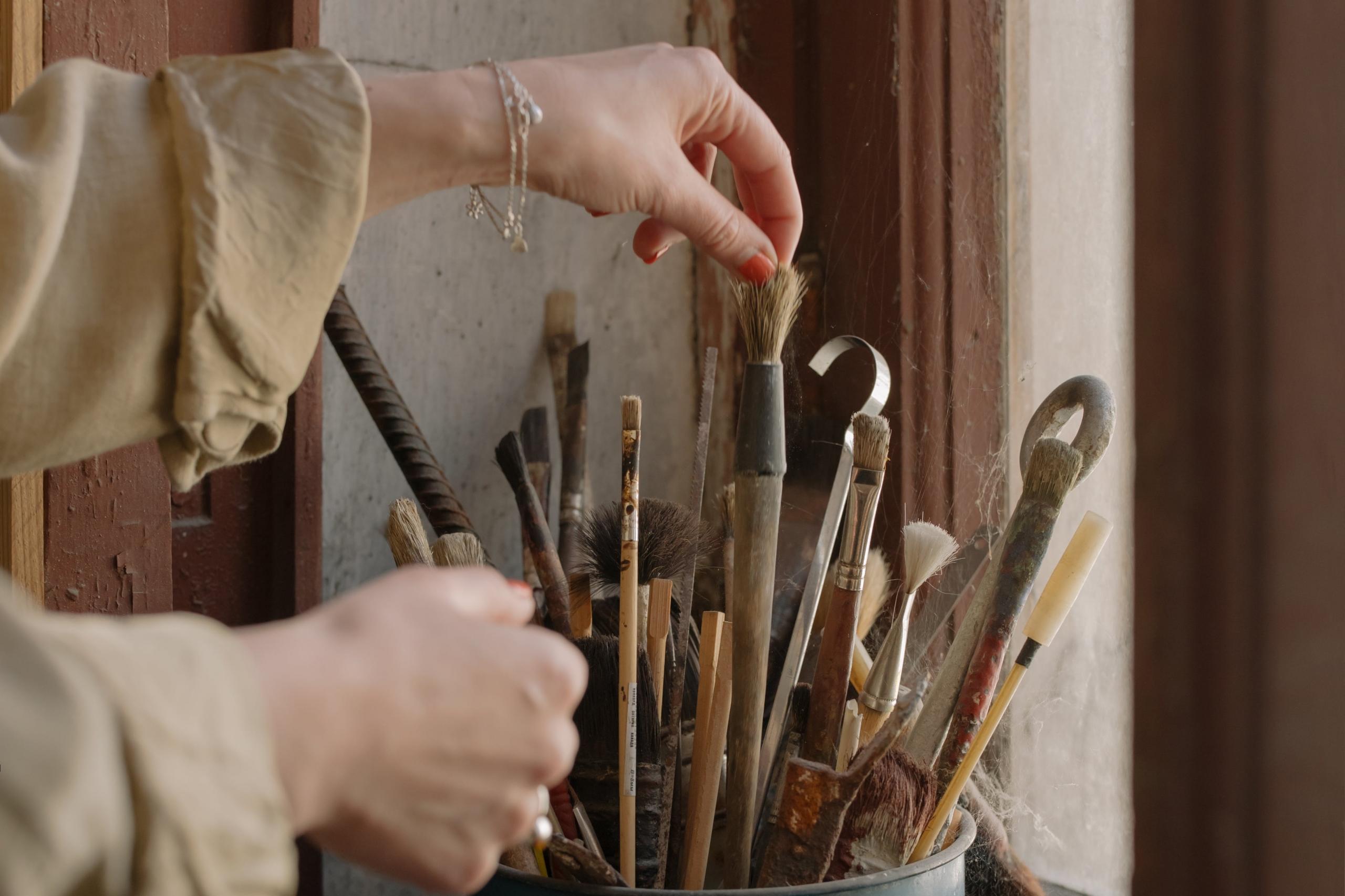 artist choosing a paintbrush from a selection placed in a paintbrush holder on windowsill