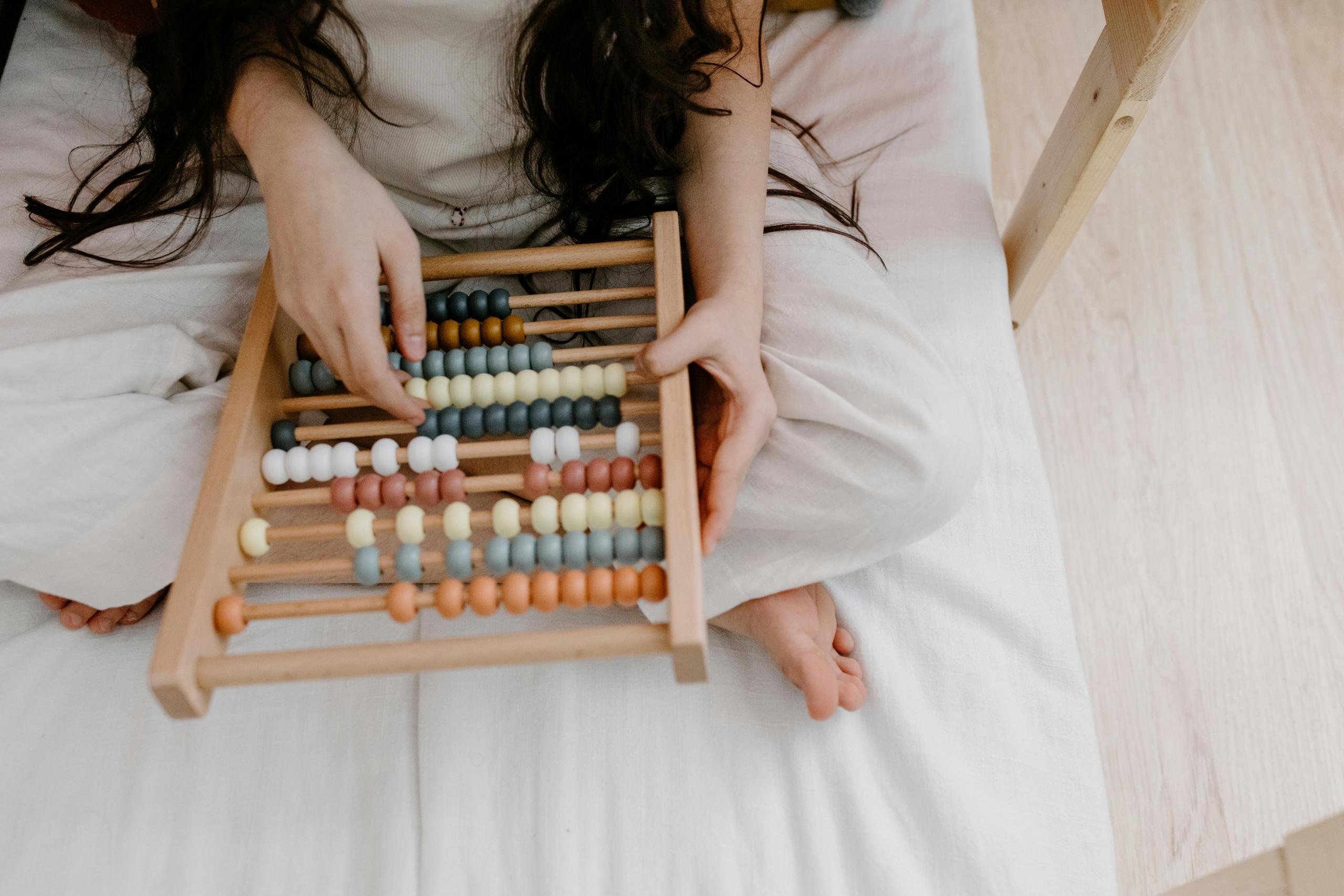 girl sitting on bed playing with wooden abacus