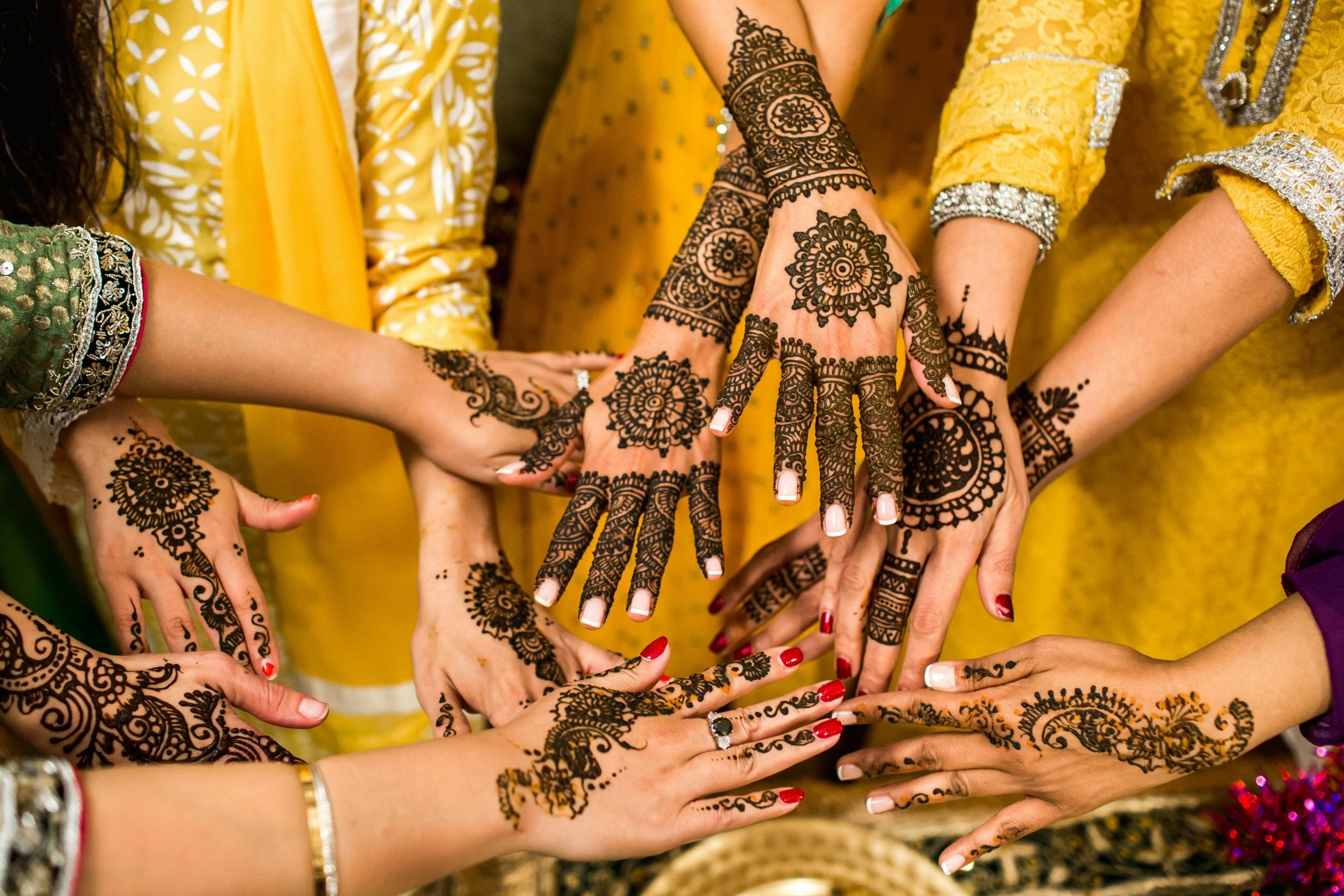 women wearing yellow saris and holding out hands decorated with henna