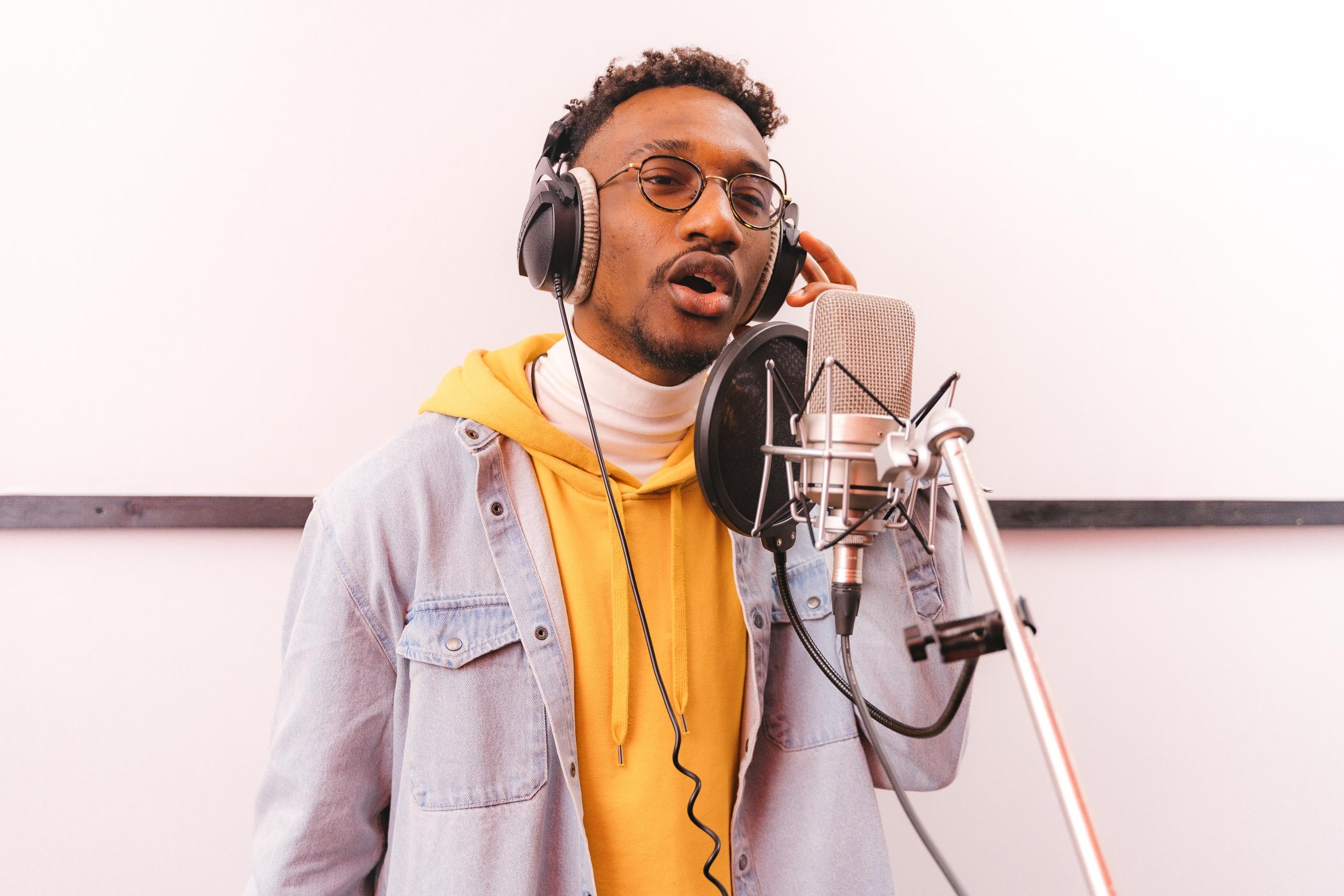 singer wearing yellow hoodie recording a song in recording studio