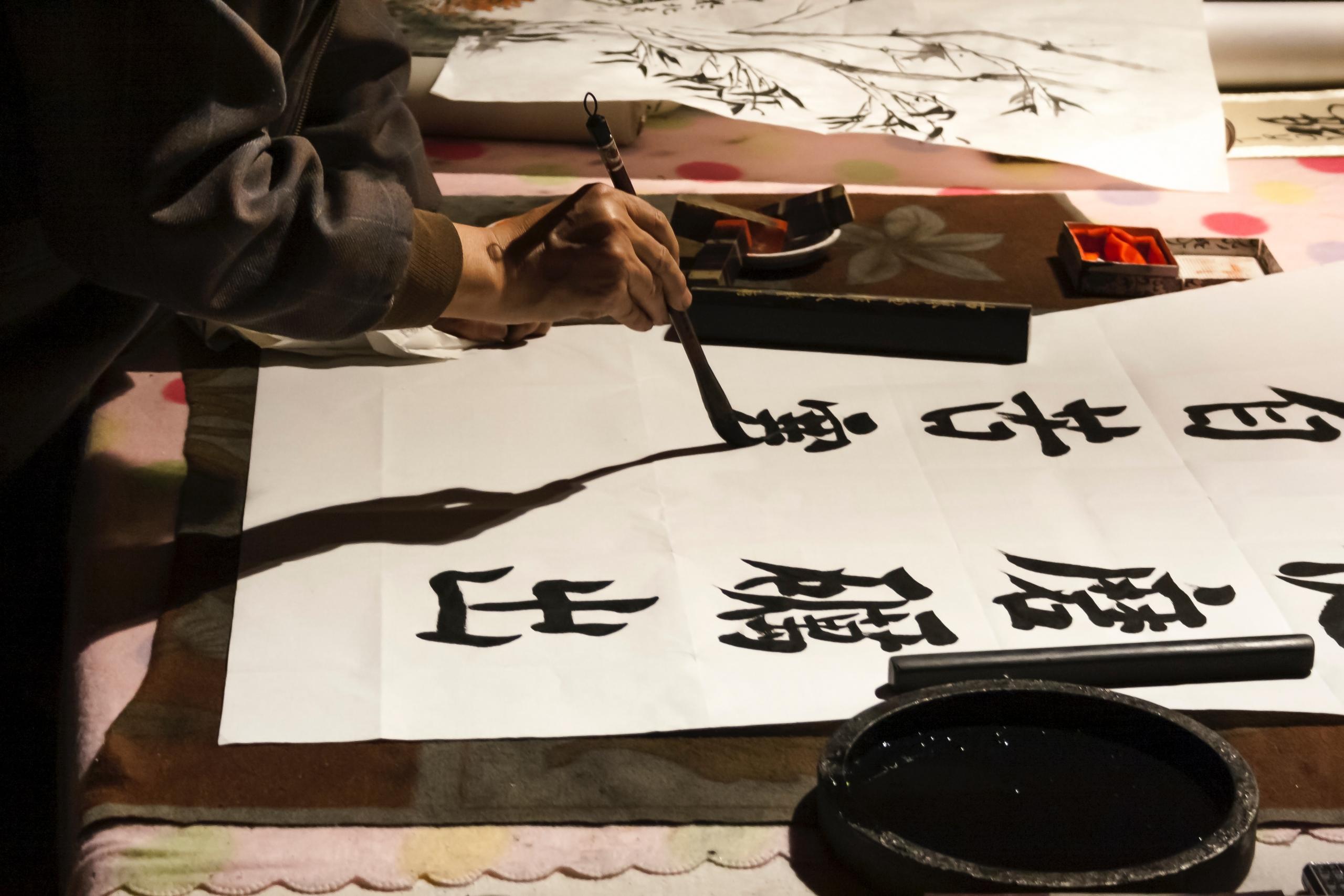 person in traditional chinese outfit doing calligraphy on large sheet of paper