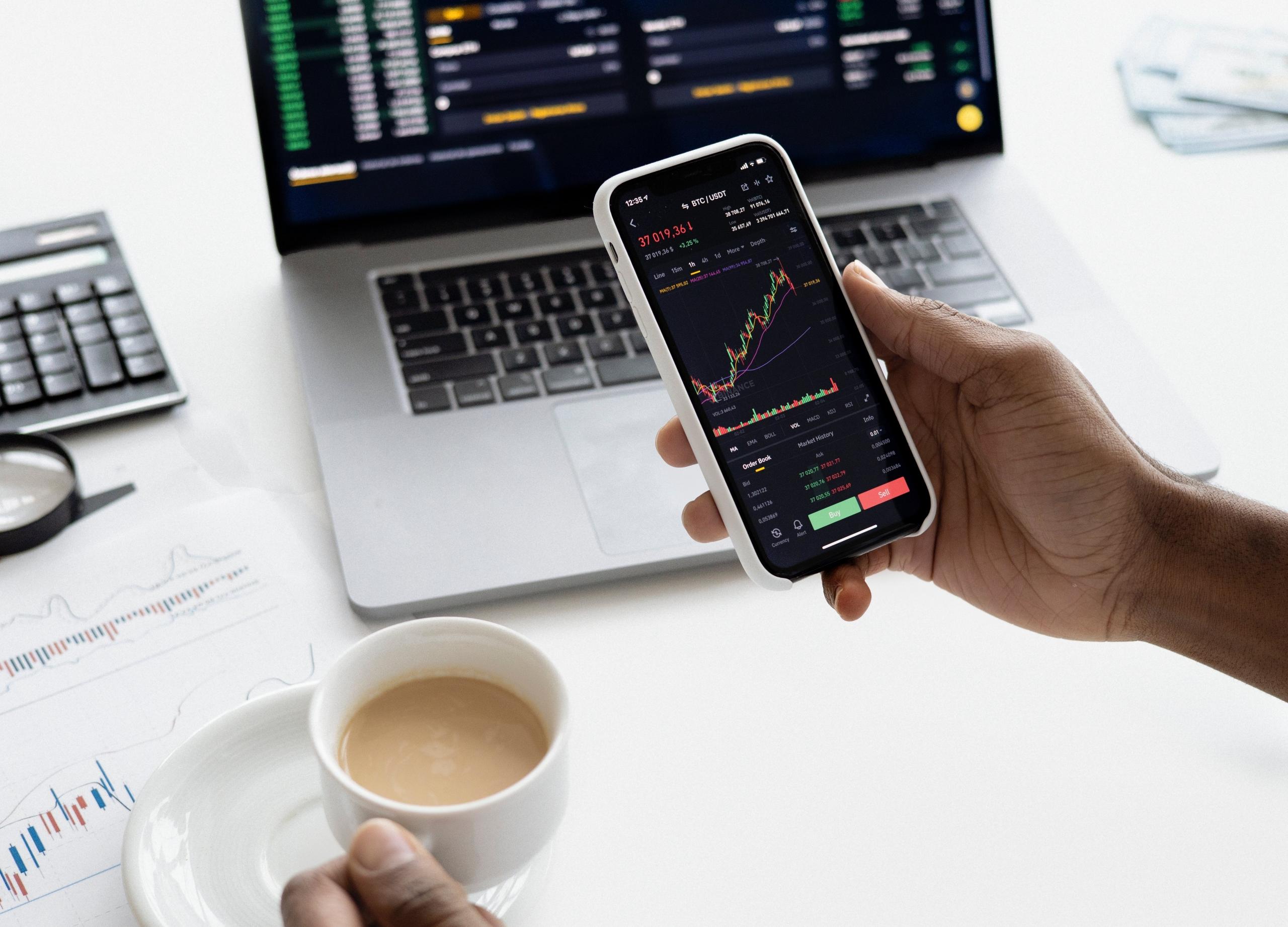 person working on laptop and checking stock market performance on phone