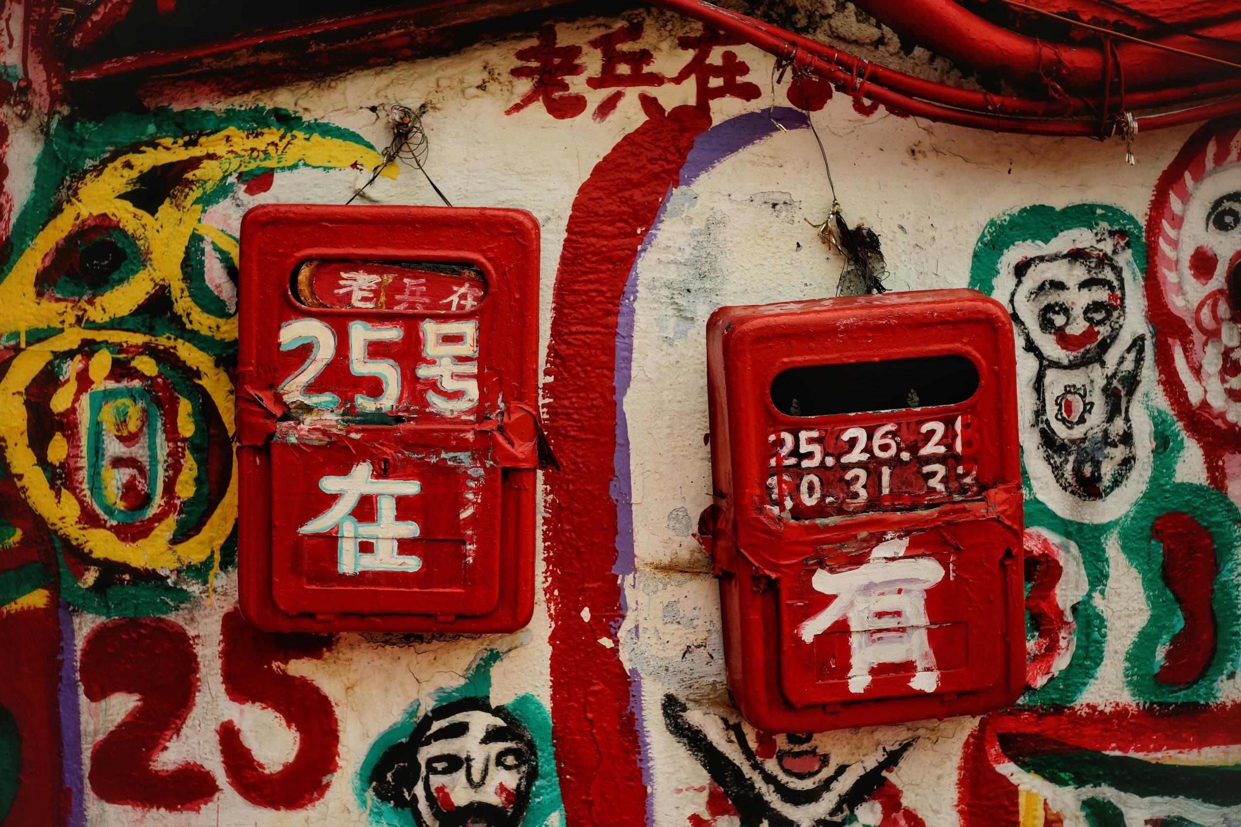 red postboxes with chinese writing on graffiti covered wall