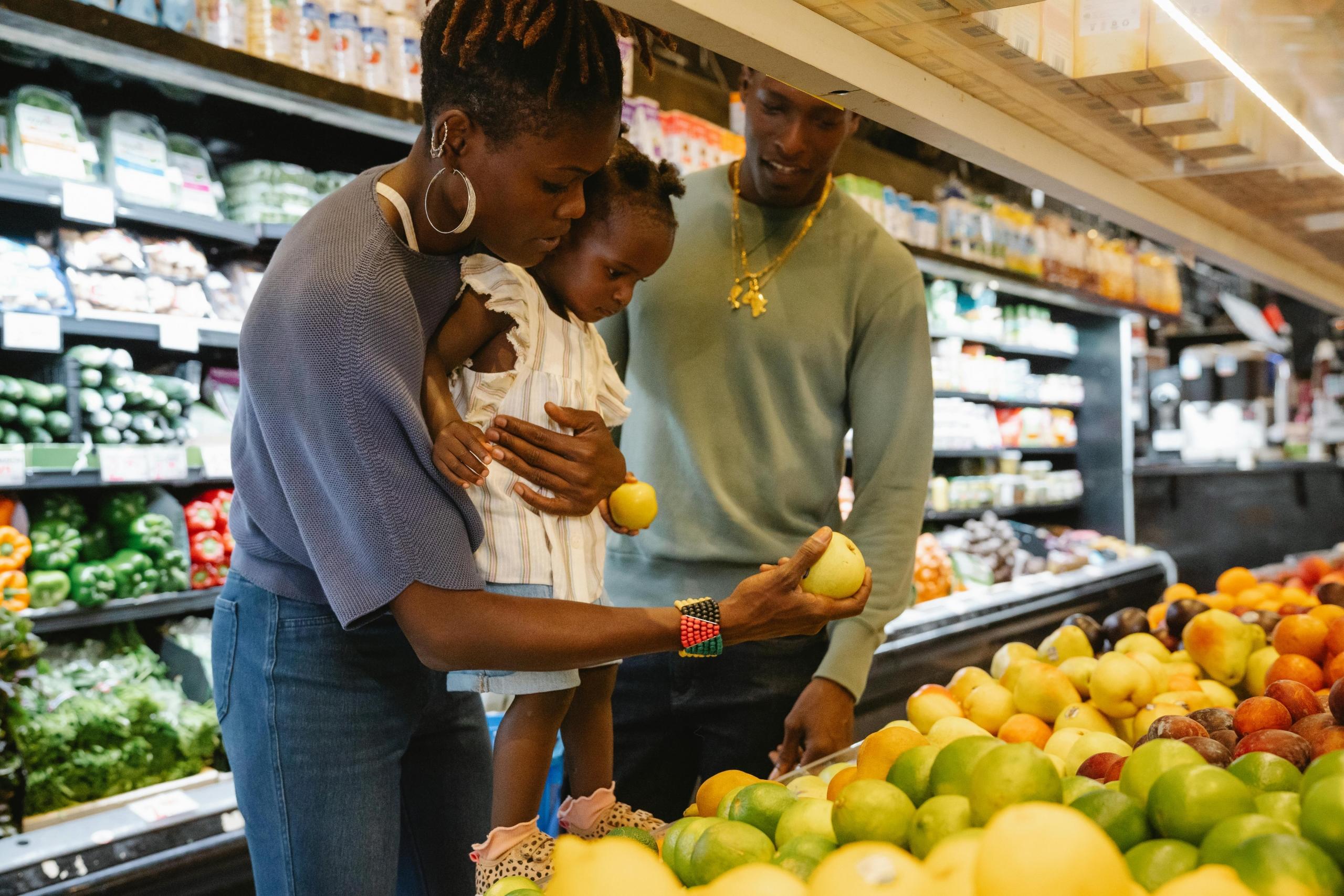 parents and small child selecting fresh fruit in supermarkets
