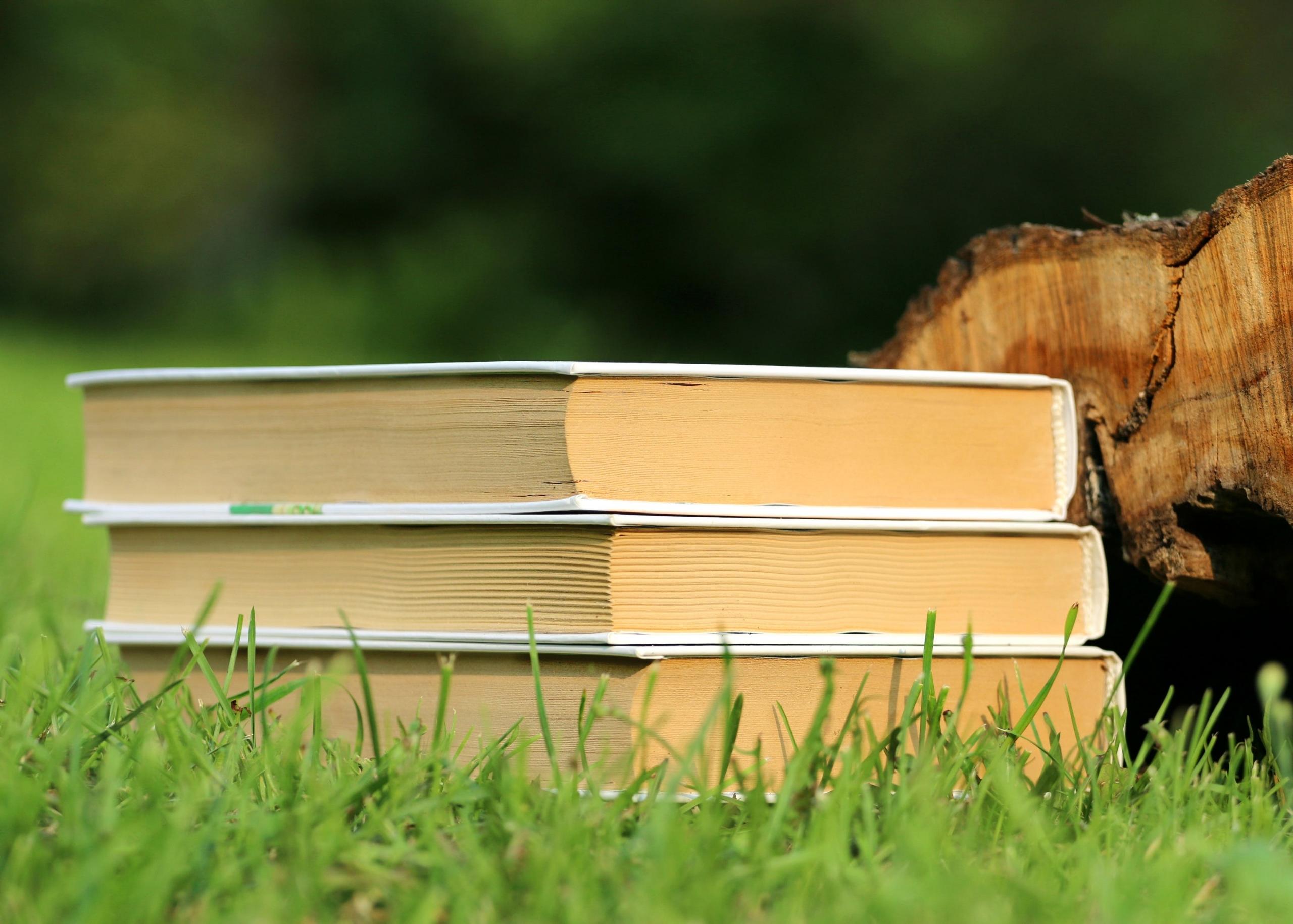 three books stacked in a pile on the grass