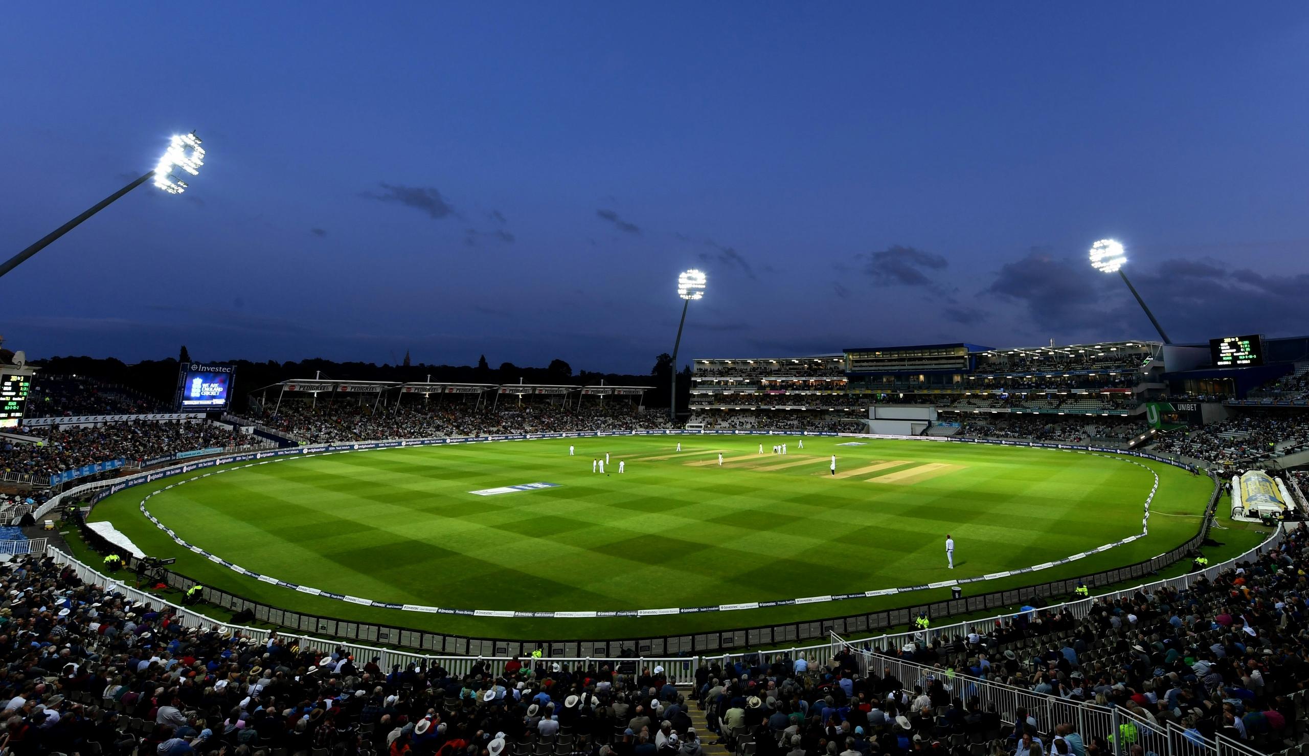 cricket game being played in a stadium at night under floodlights