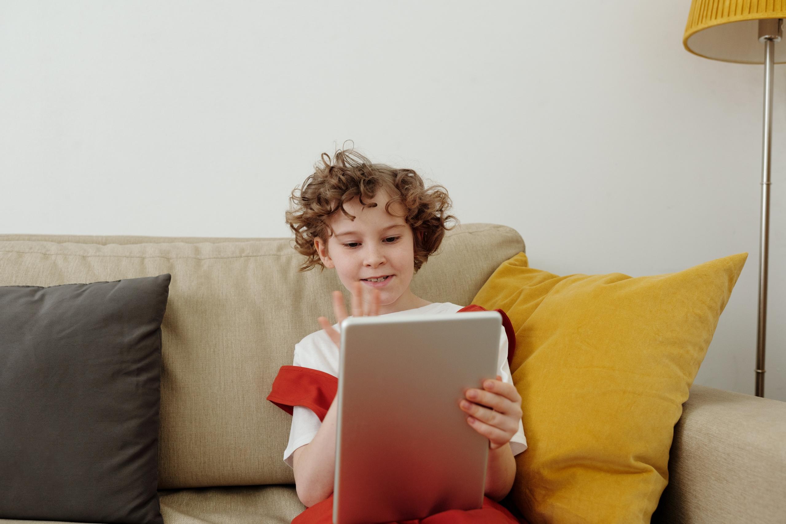 boy sitting on couch making video call on tablet