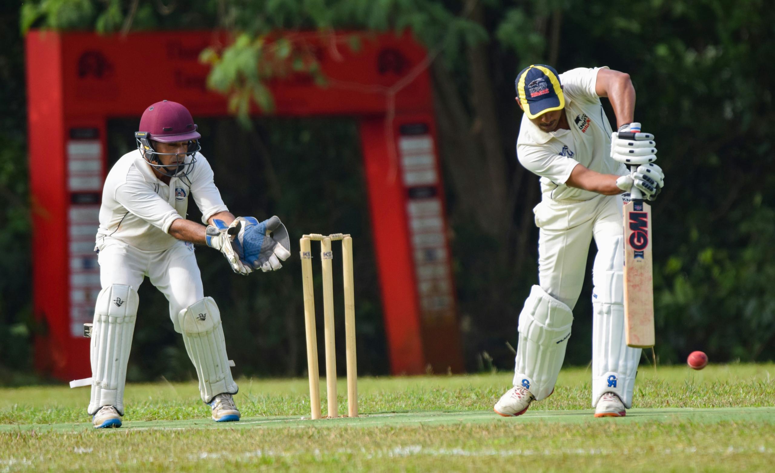 cricket batsman hitting ball with wicket keeper standing behind wickets