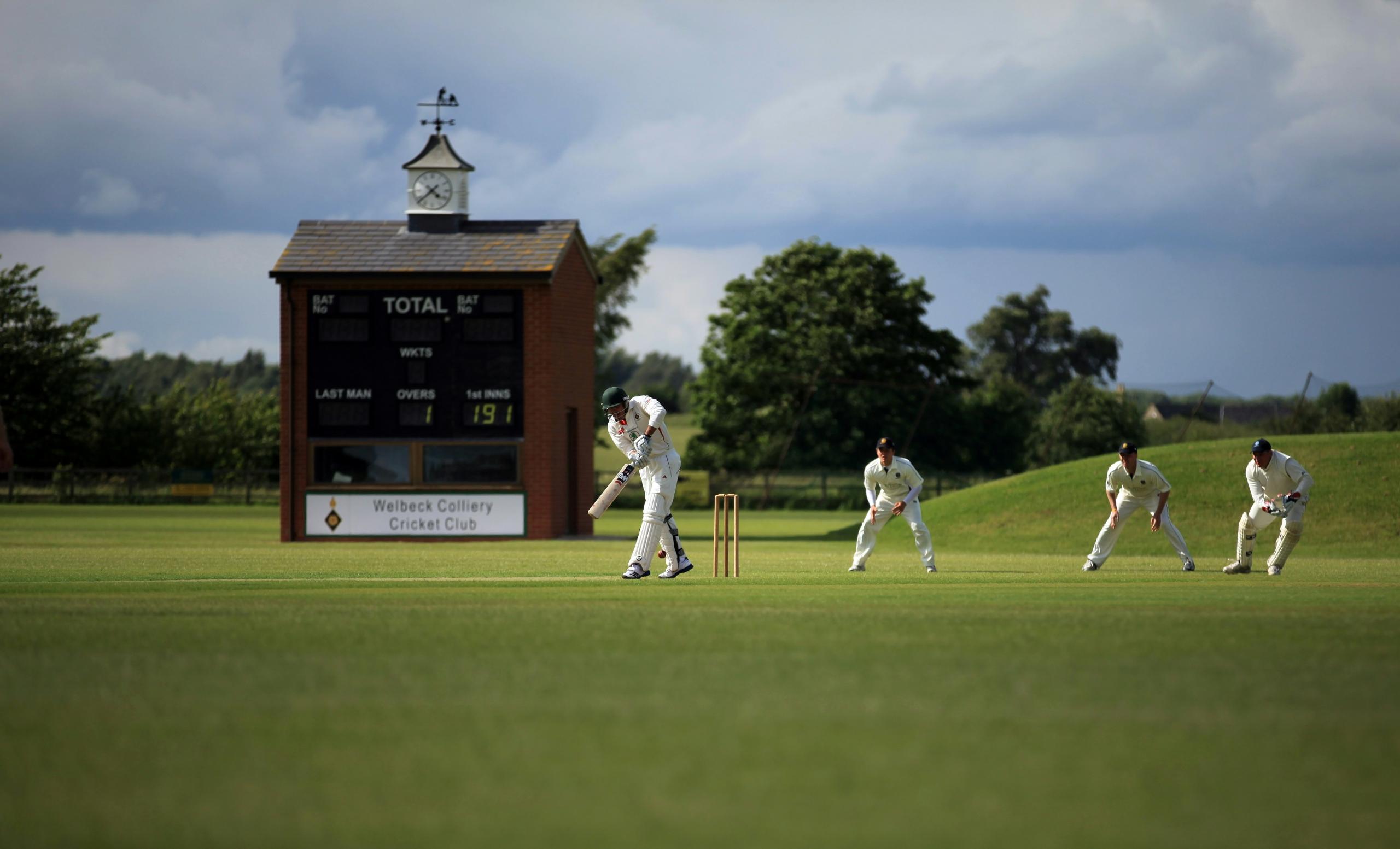 cricket players fielding and batting near giant wooden scoreboard