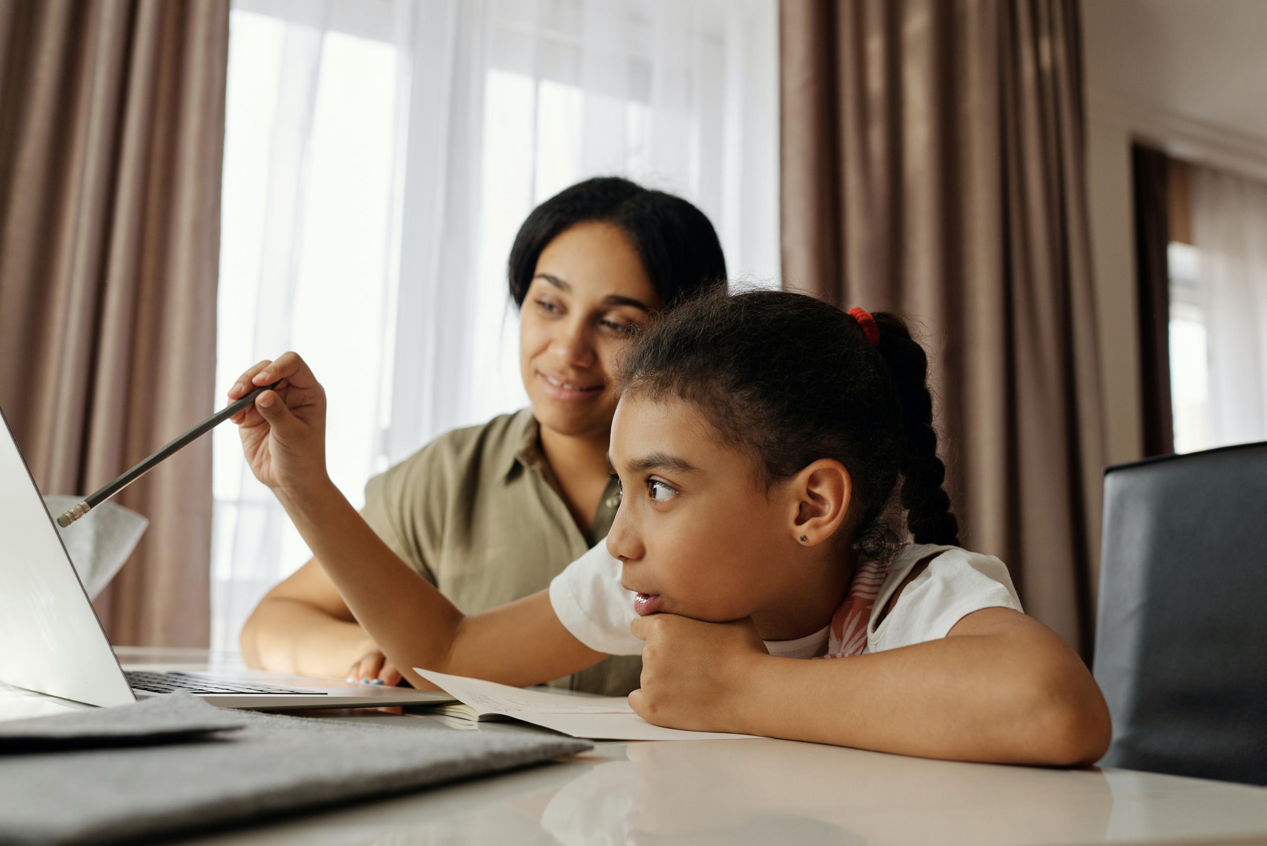 child taking online lessons while her mom supervises